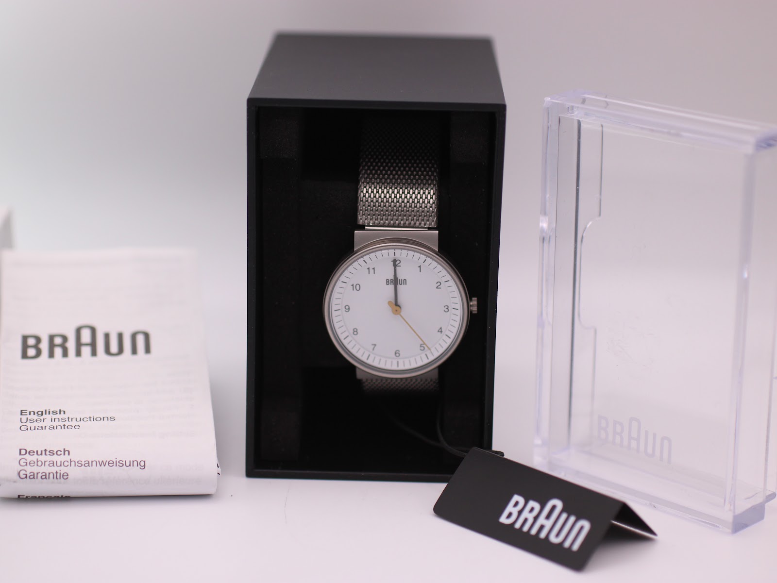 Front view of the Braun BN0031WHSLMHL watch with a clean white dial, black Arabic numerals, and a silver mesh bracelet.