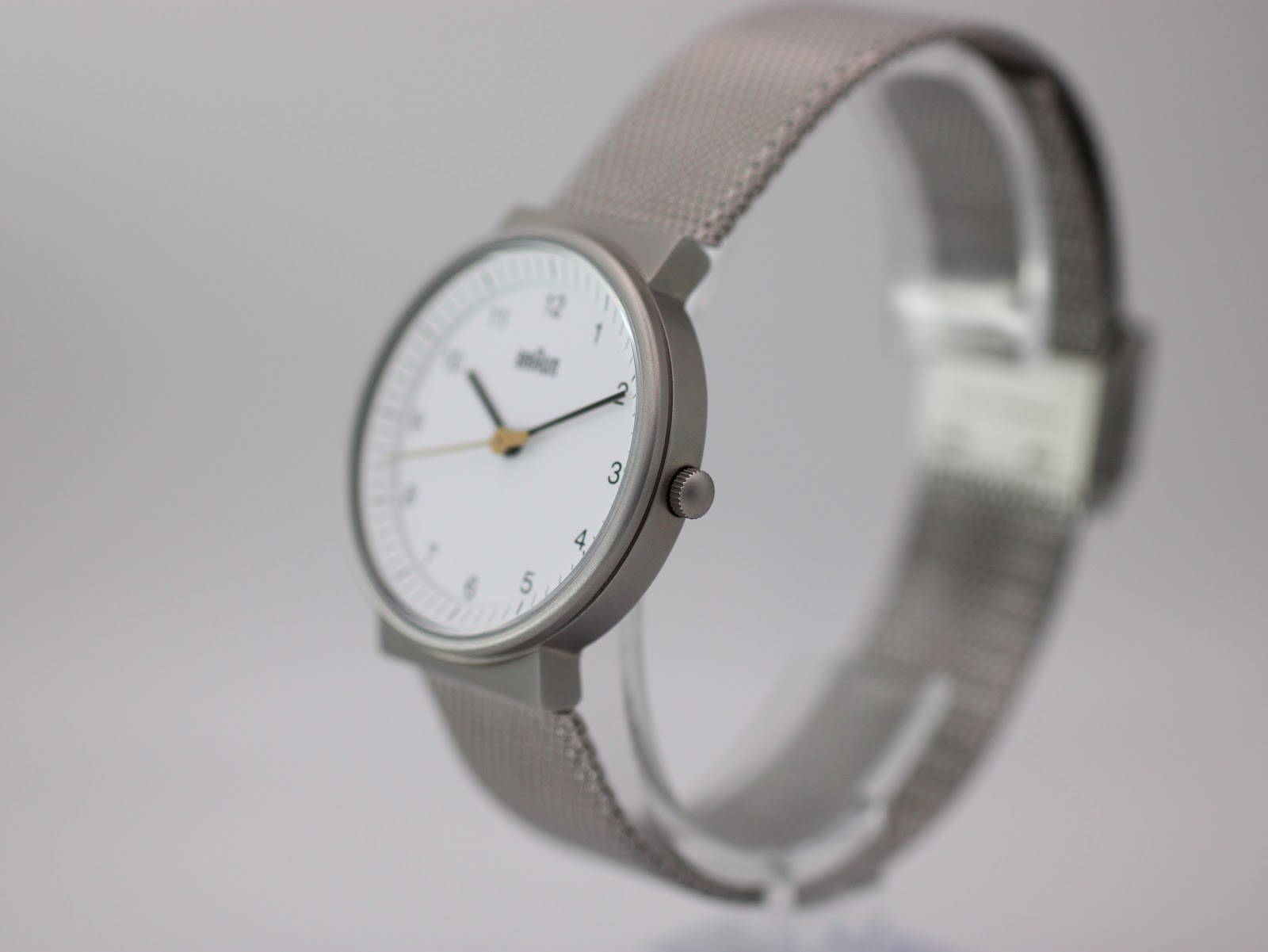 Angled side view of the Braun watch on a display stand, showcasing its minimalist silver case and the texture of the mesh bracelet.