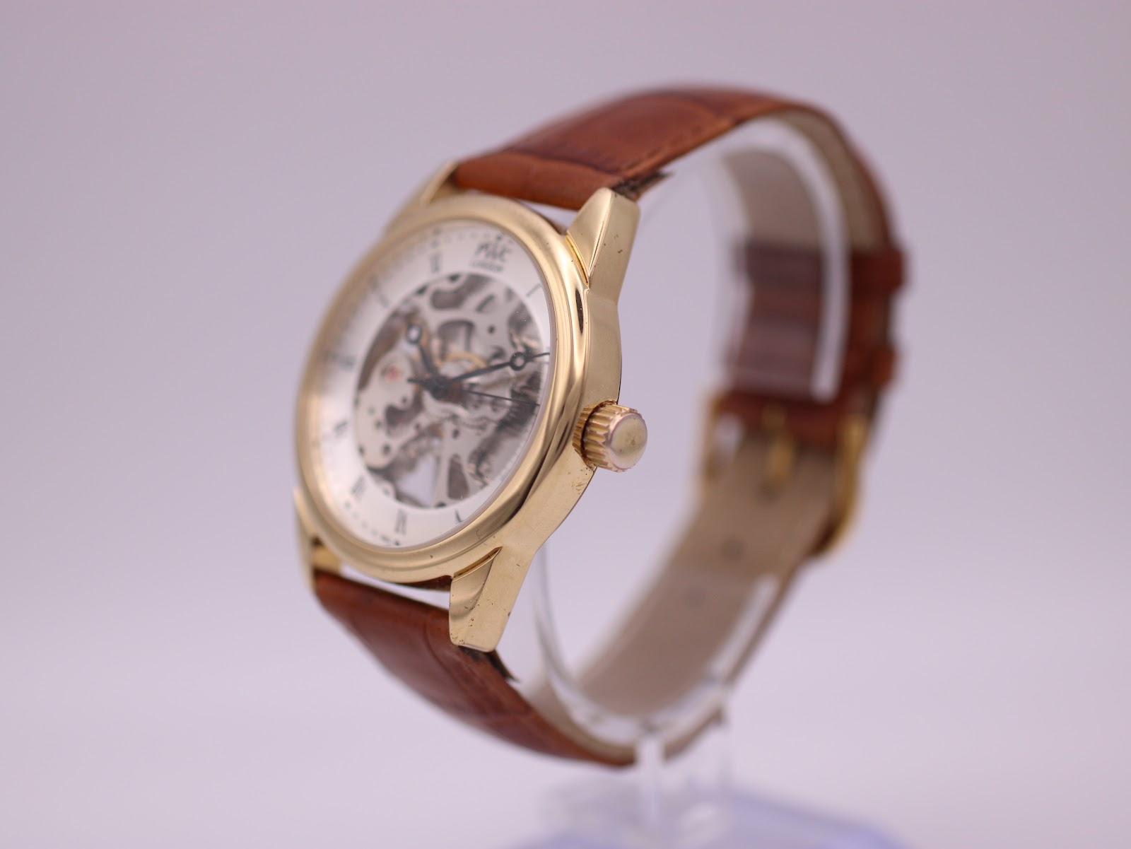 Angled side view of the PWC London watch from the right, highlighting the gold-tone case, crown, and brown leather strap