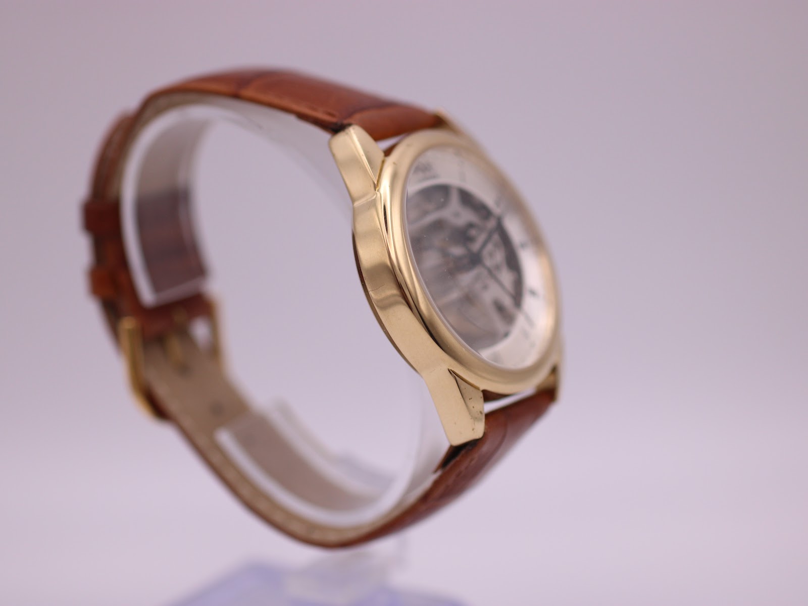 Angled side view of the PWC London watch from the left, showcasing the sleek profile of the gold-tone case