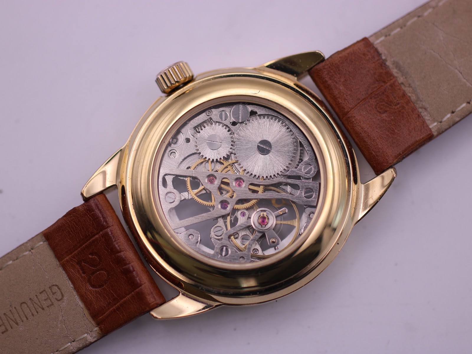 Rear view of the PWC London watch with an exhibition case back, displaying the manual wind movement and the 'Genuine Leather' stamped strap