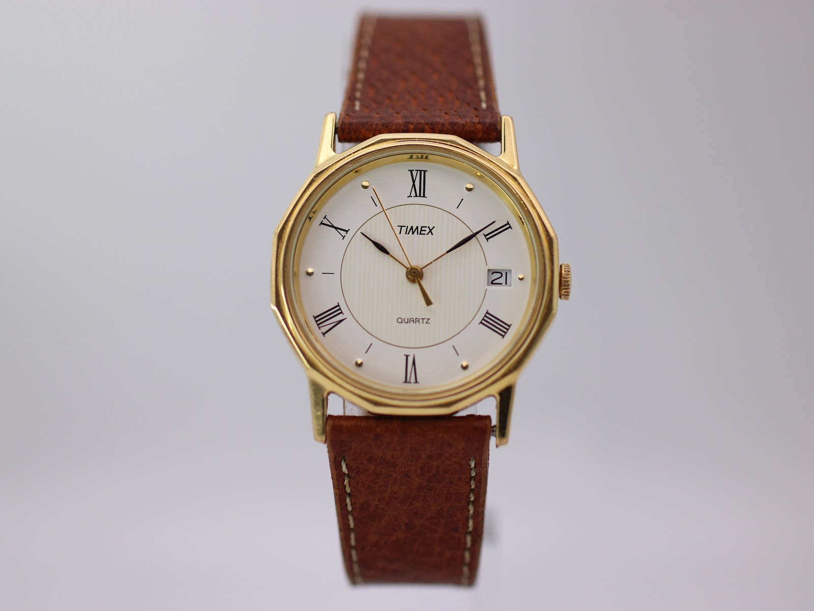 Front view of gold-tone Timex octagonal quartz watch with cream dial and brown leather strap.