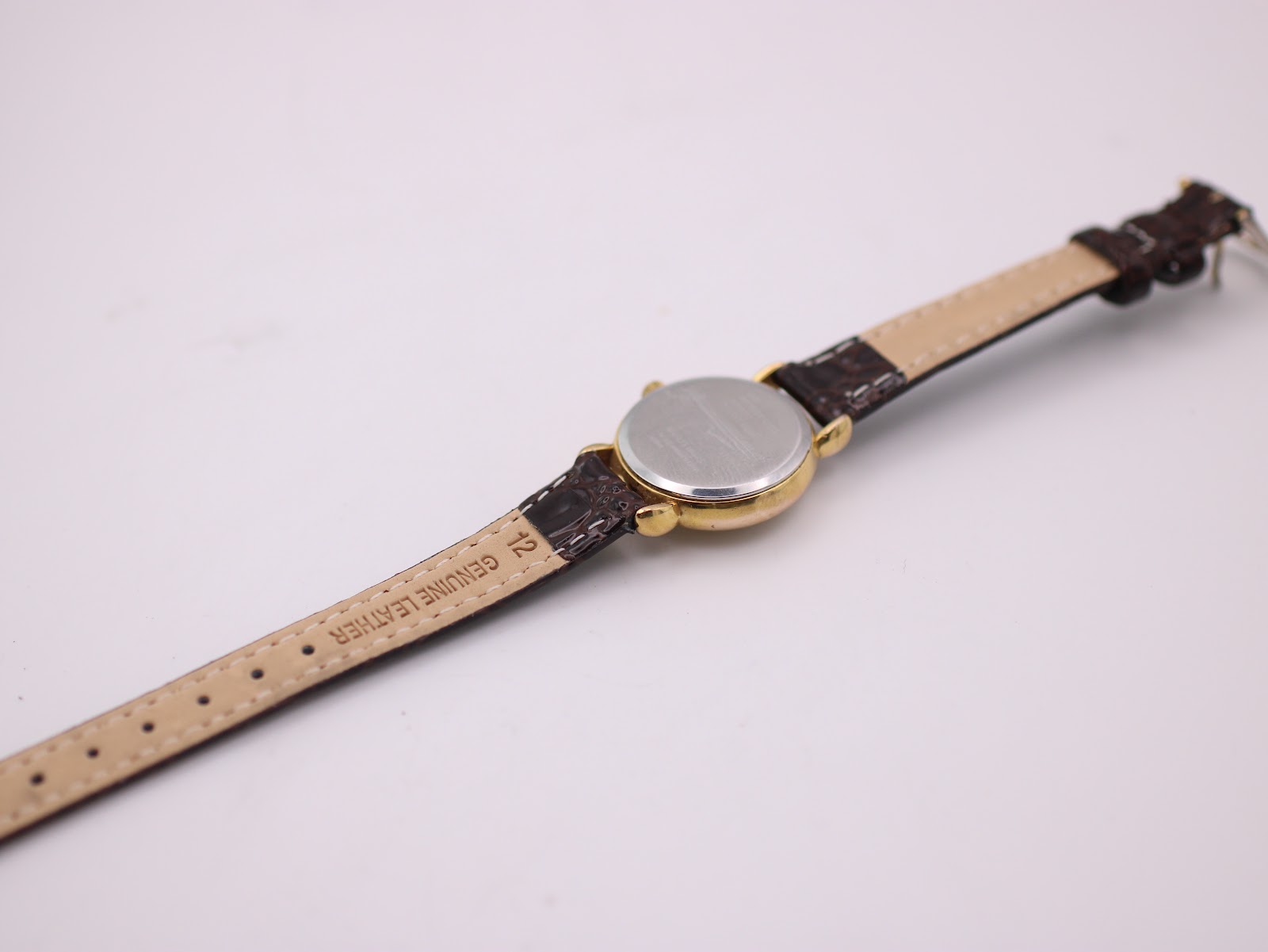 Back view of the watch and the underside of the brown leather strap, showing 'genuine leather' marking.