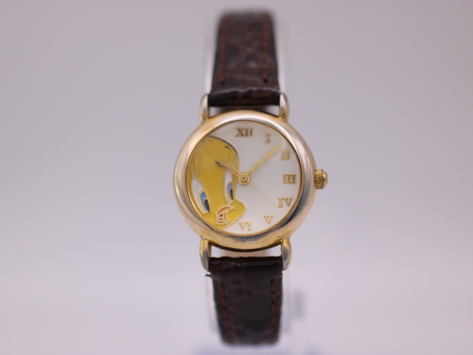 Front view of the gold-tone Warner Bros. Tweety Bird watch with a white dial and brown leather strap on a watch stand.