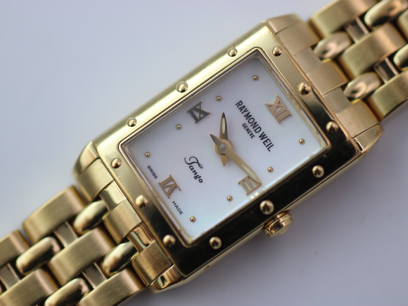Close-up front view of the Raymond Weil Tango dial, showing Roman numerals, gold hands, and mother-of-pearl texture.