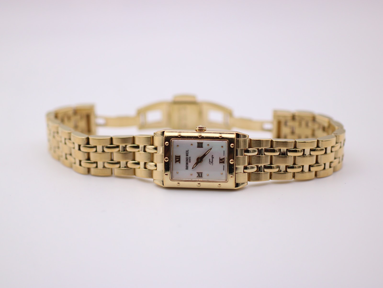 Full front view of the gold Raymond Weil Tango watch with its integrated bracelet laid flat on a light background.