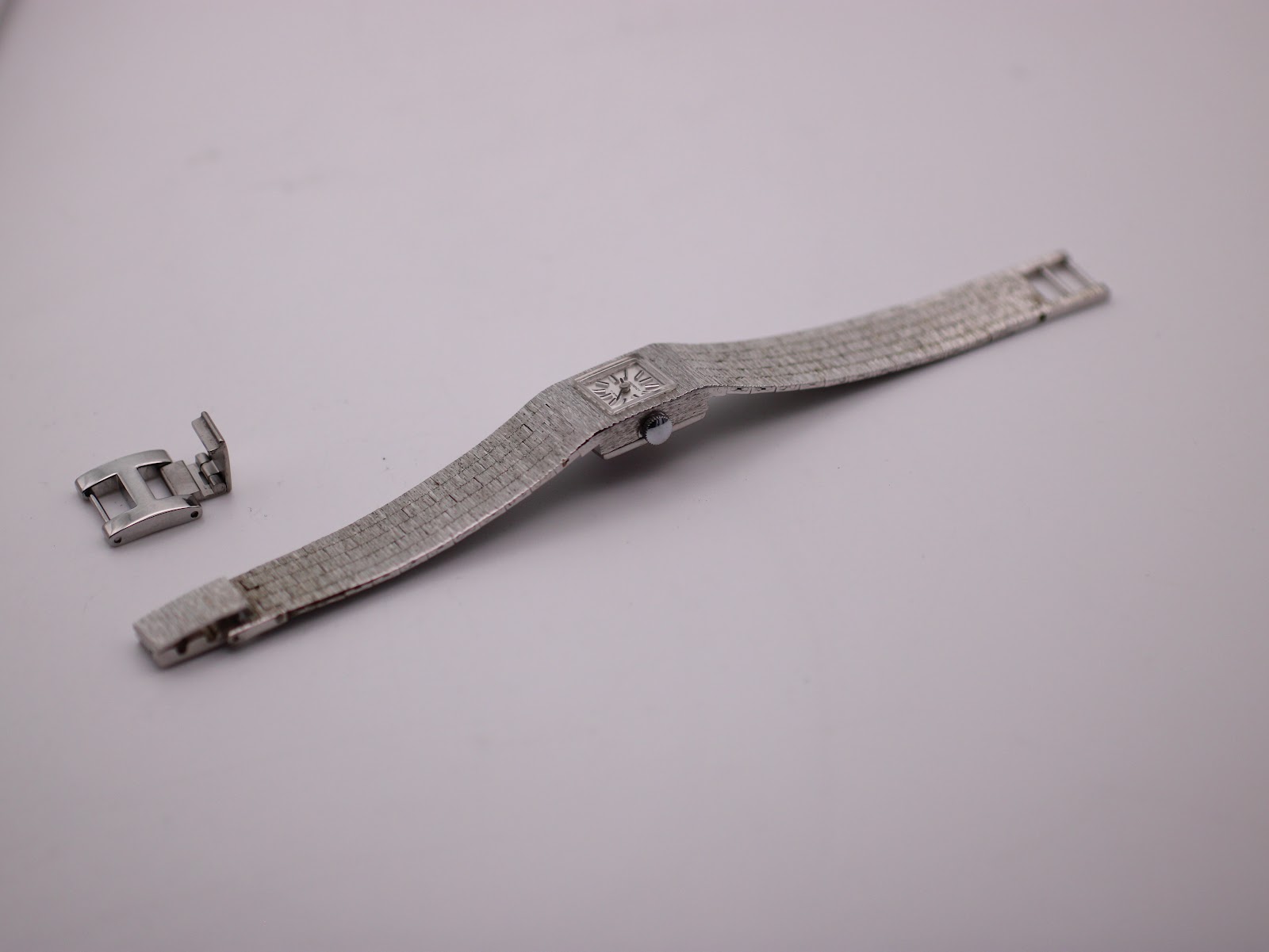 Overhead view of the watch and detached clasp, showing the full length of the integrated bracelet.
