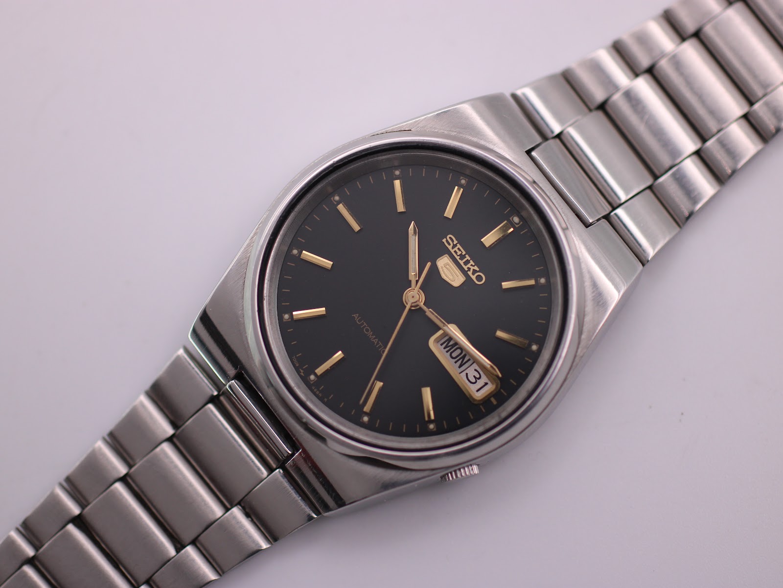 Top-down view of the Seiko 7009-3130 watch with black dial, day-date display, and stainless steel bracelet.