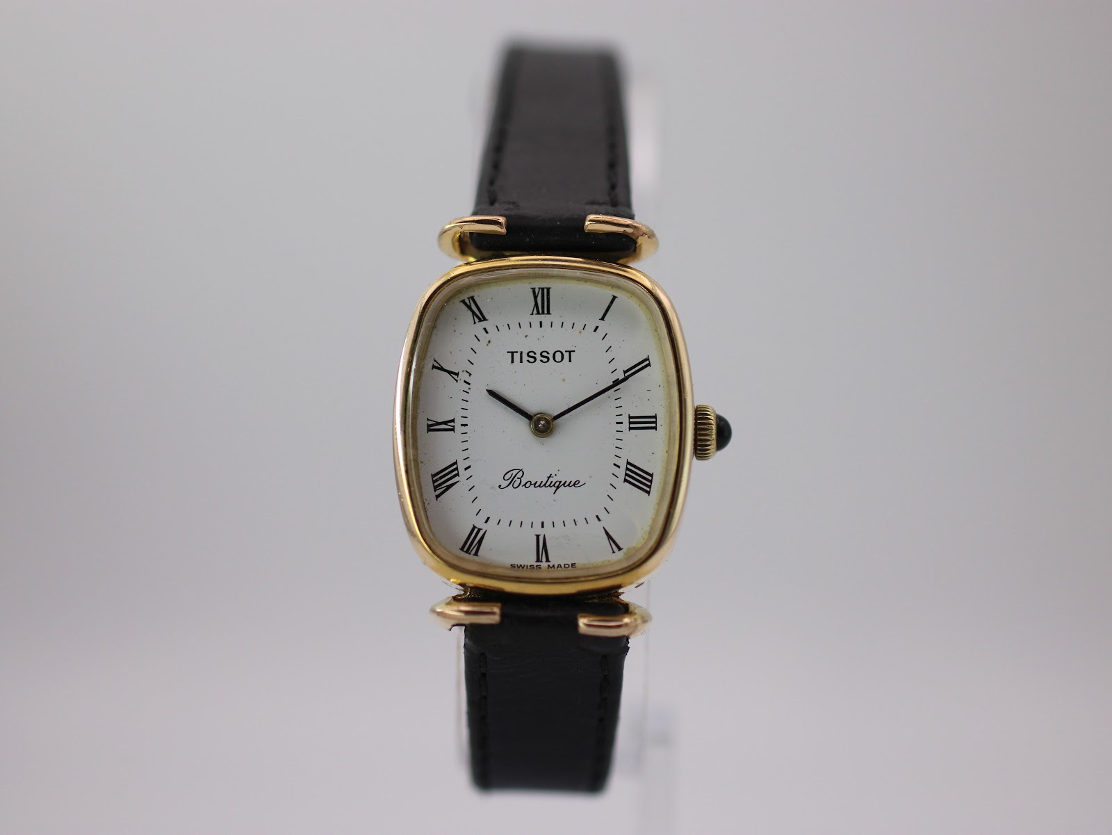 Front view of the Tissot Boutique watch, showing the gold tone cushion case and white dial with Roman numerals.