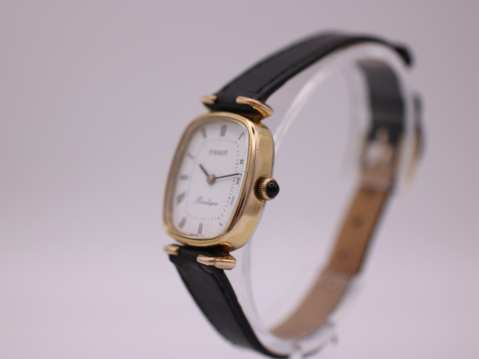 Angled side view of the Tissot Boutique watch, showing the gold tone case, black crown, and black leather strap.