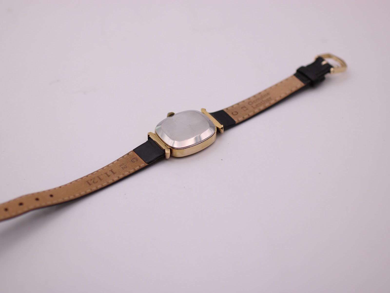 View of the watch from the rear, showing the plain metal case back and the underside of the black leather strap.