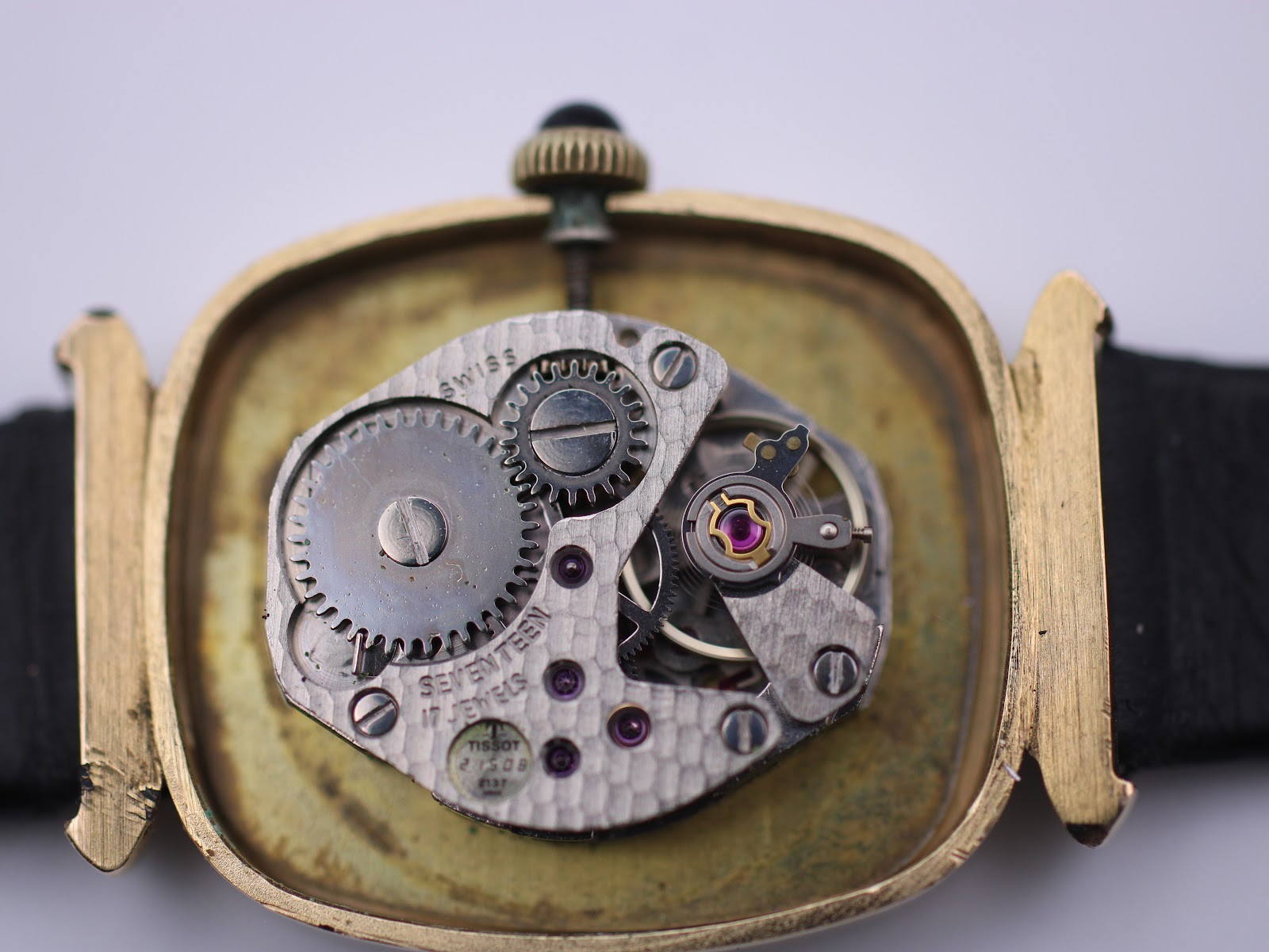 Open case back revealing the Tissot manual wind movement with visible gears and jewels.