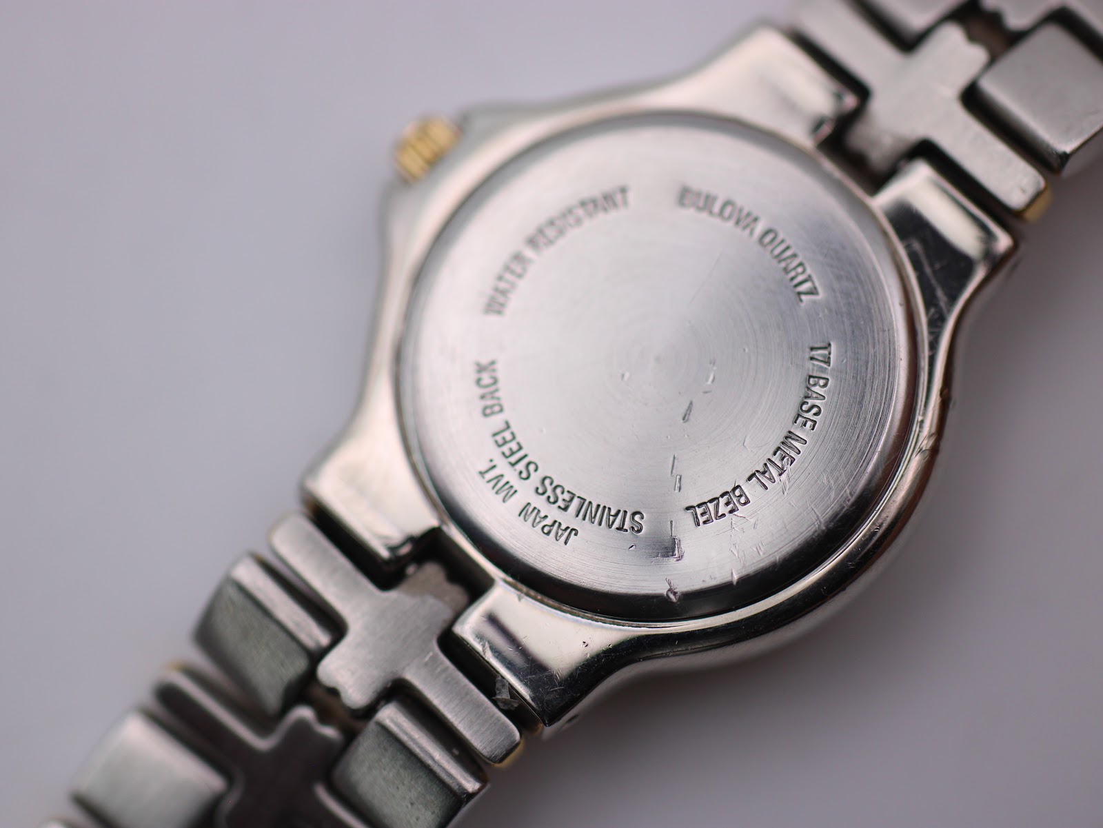 Close-up of the watch's stainless steel case back, engraved with "STAINLESS STEEL BACK", "JAPAN MVT", "BULOVA QUARTZ", and "TT BASE METAL BEZEL".