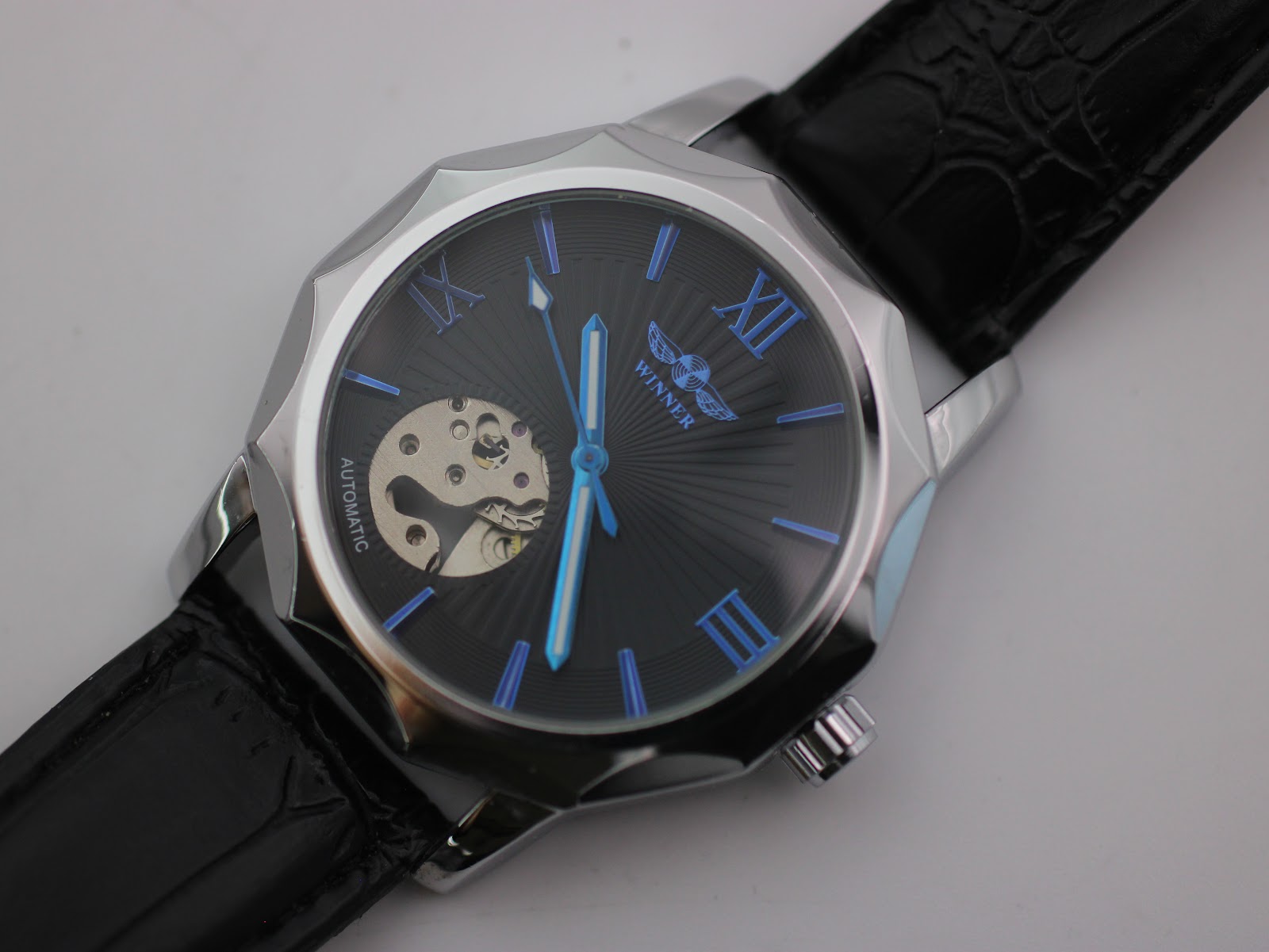 Close-up top-down view of the Winner H199M black sunburst dial with blue Roman numerals, stick indices, and automatic movement visible.