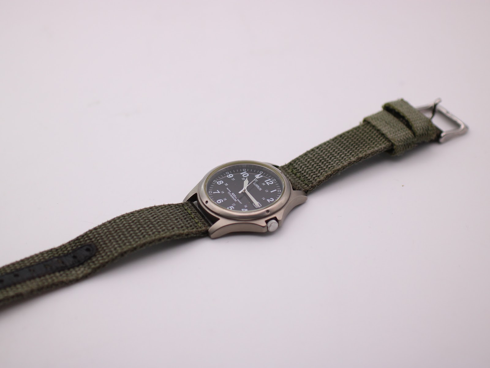 Full length view of Lorus watch with green fabric strap laid out.