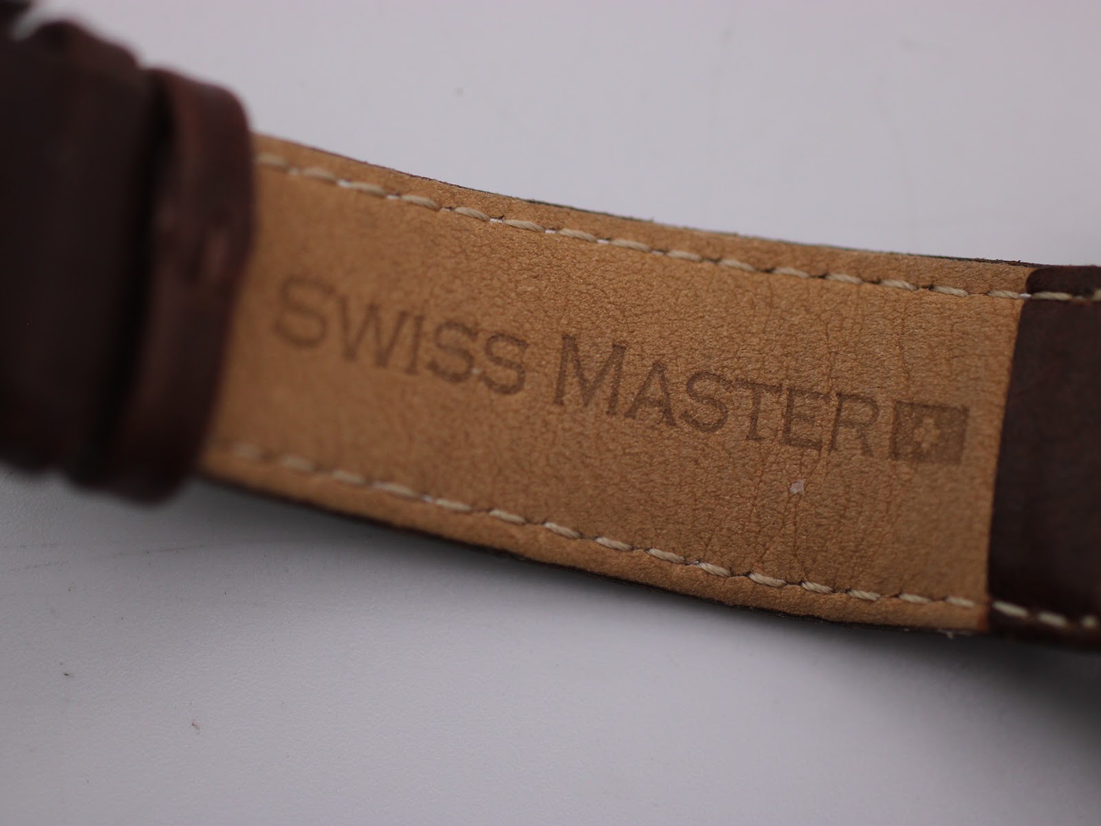 Close-up of the inner side of the brown leather strap, showing the embossed 'SWISS MASTER' logo.