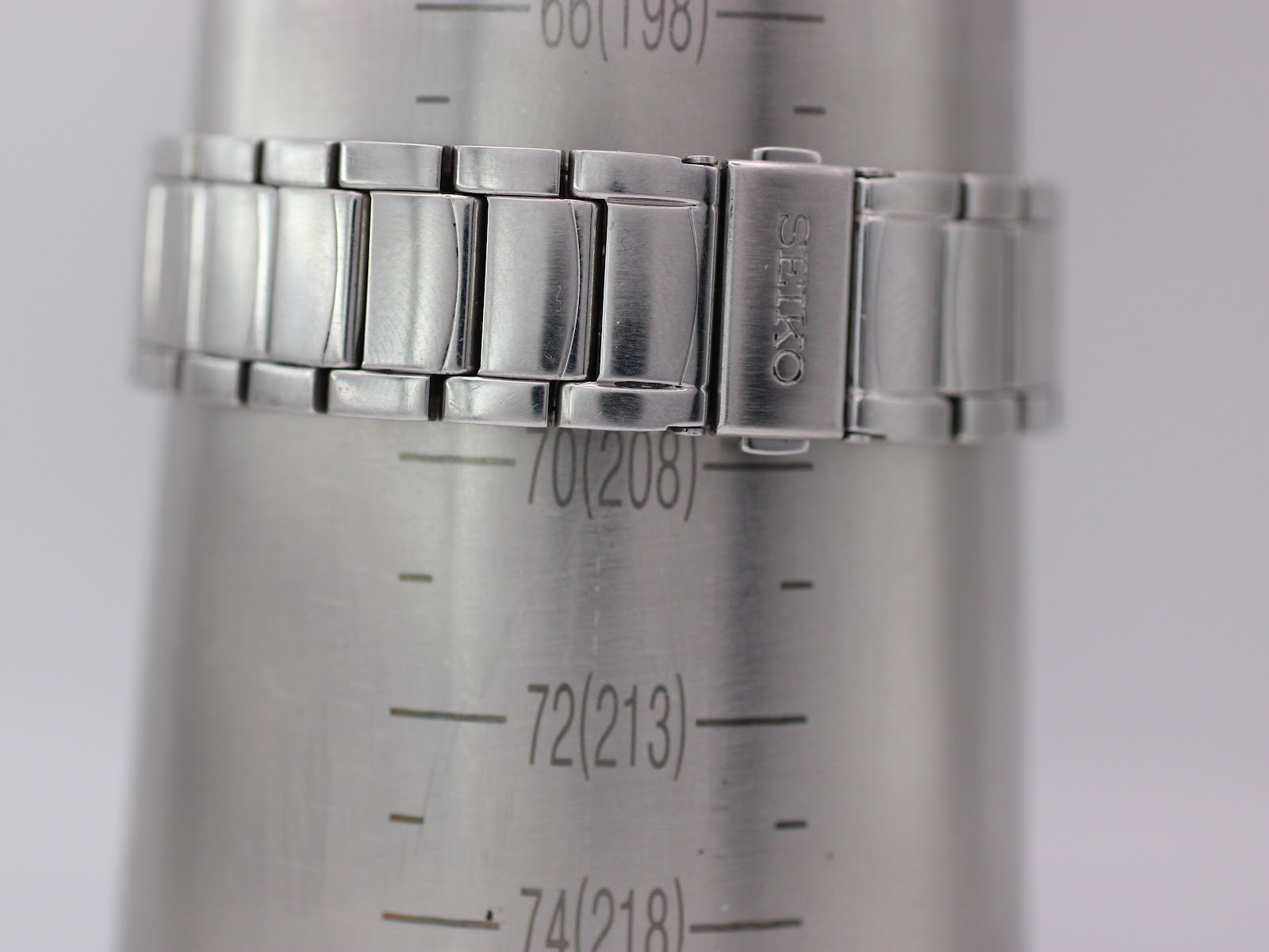 Close-up of the signed Seiko fold-over clasp on a wrist sizing gauge, showing a wrist circumference reading of approximately 20.8cm.