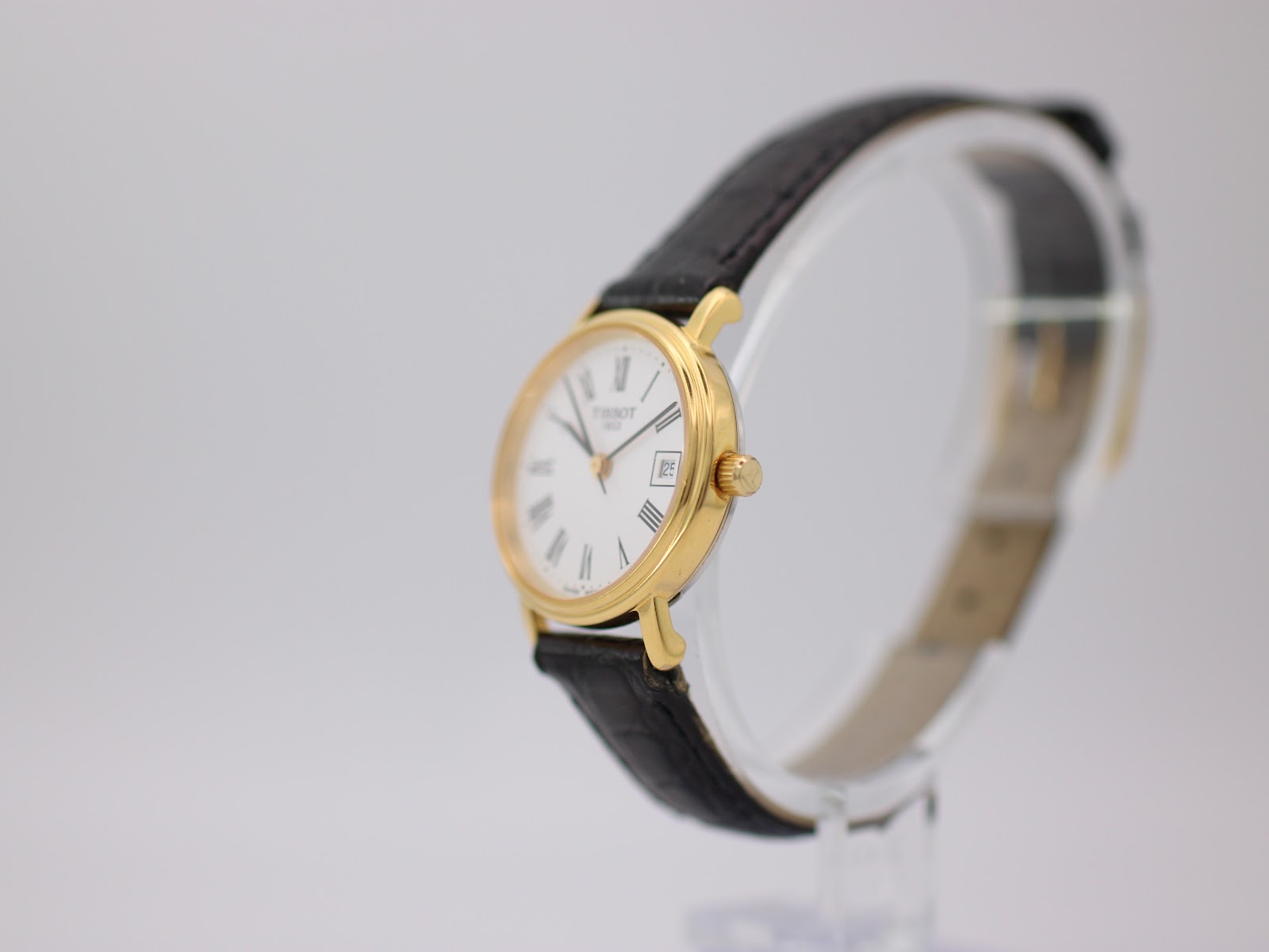 Angled side view of the Tissot watch on a display stand, highlighting the gold case and a glimpse of the black leather strap.