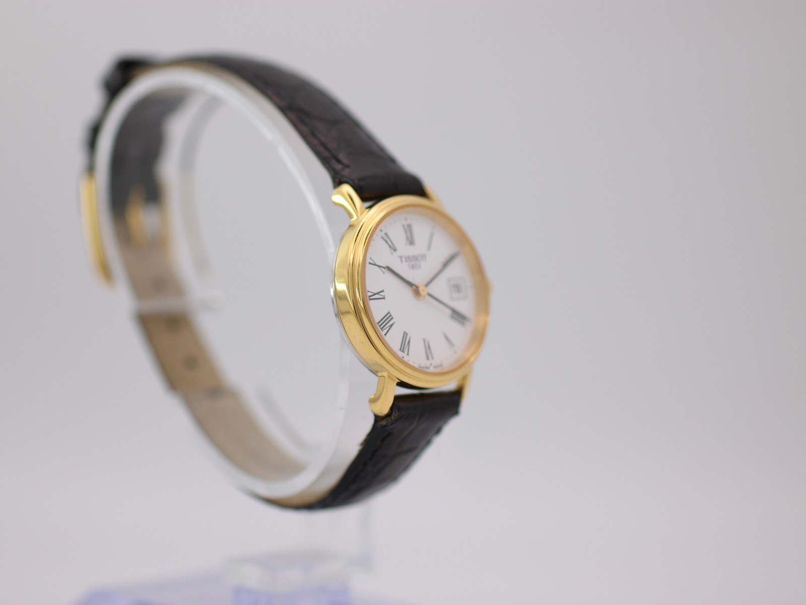 Another angled side view of the gold Tissot watch on a display stand, showing the crown and the strap.