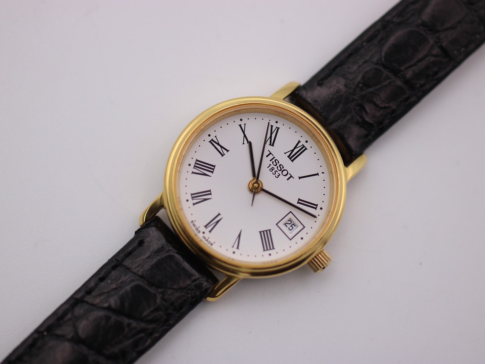 Top-down view of the Tissot watch, focusing on the white dial with Roman numerals, date window, and black crocodile-grain leather strap.
