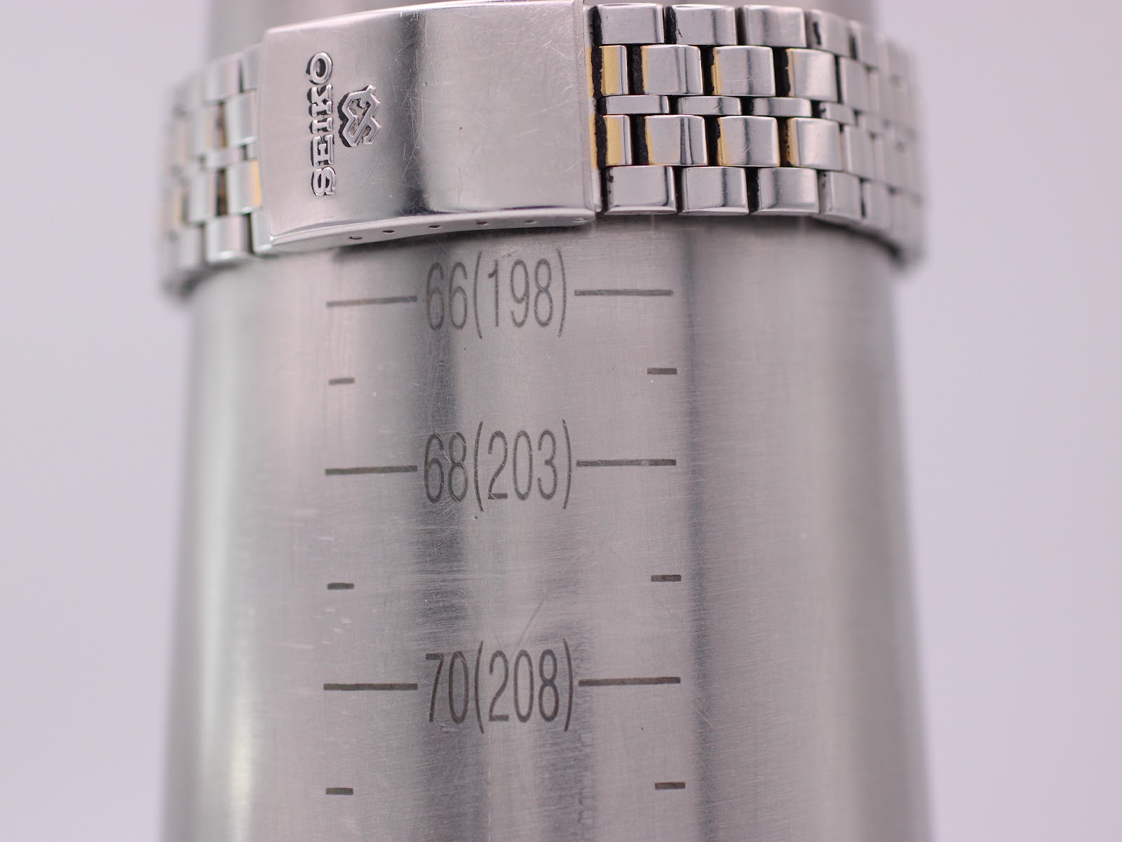 Close-up of the Seiko SQ 100 bracelet on a wrist sizing gauge, indicating a fit up to 203mm.