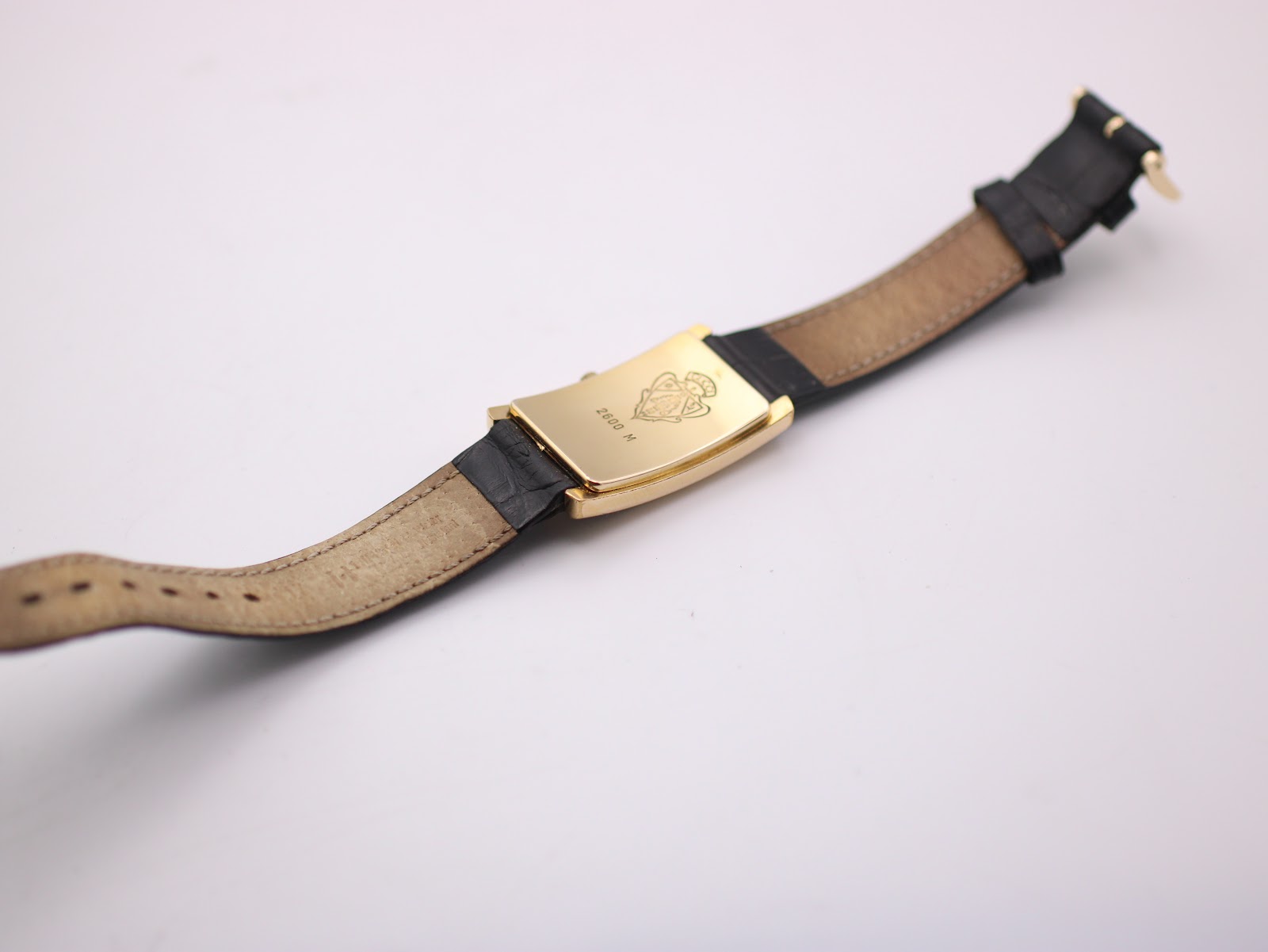 Reverse full view of the Gucci watch, showing the underside of the black leather strap and the detailed gold-tone case back.