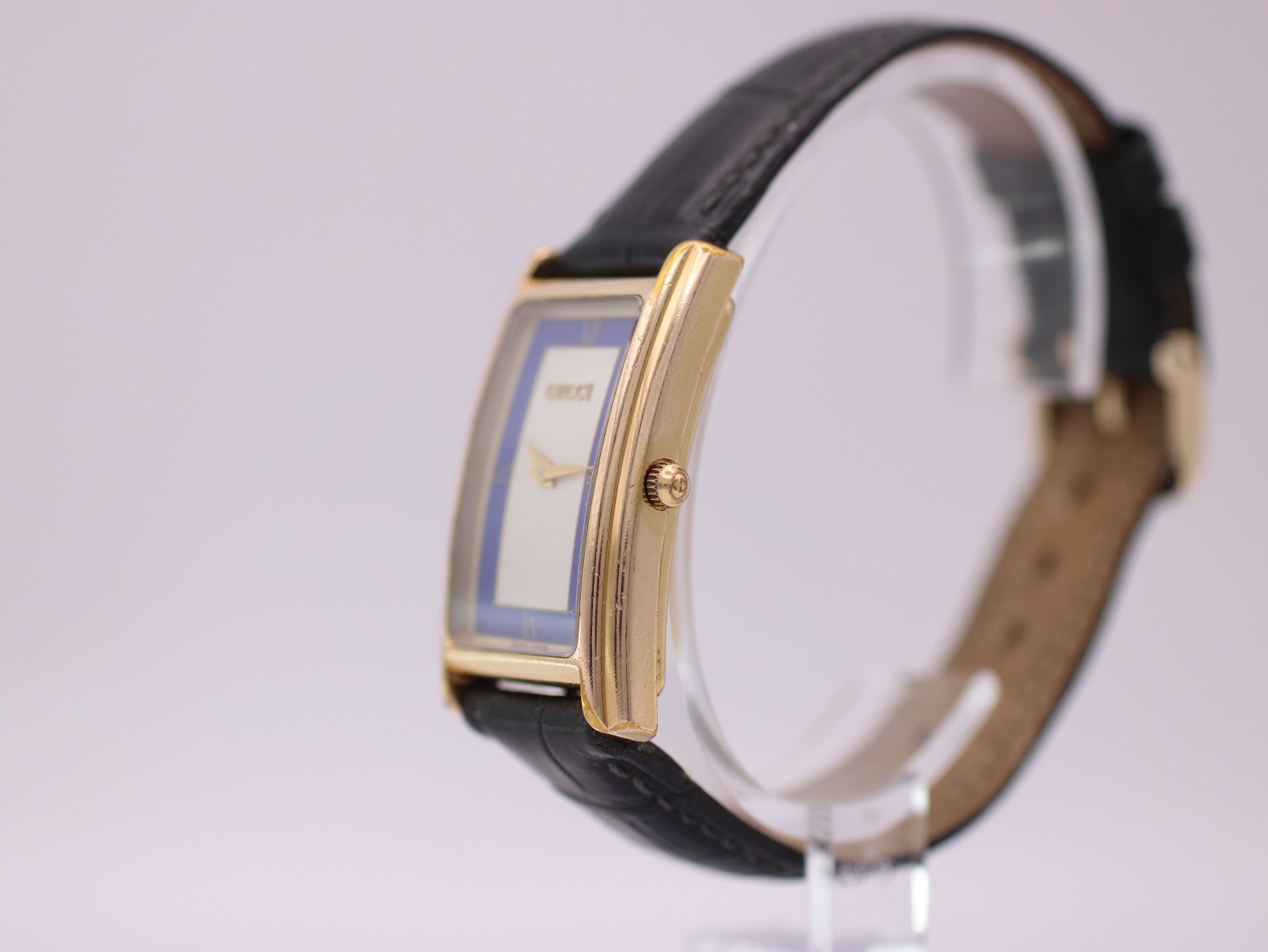 Side profile view of the Gucci 2600 M watch, showcasing the curved gold-tone case and textured crown.
