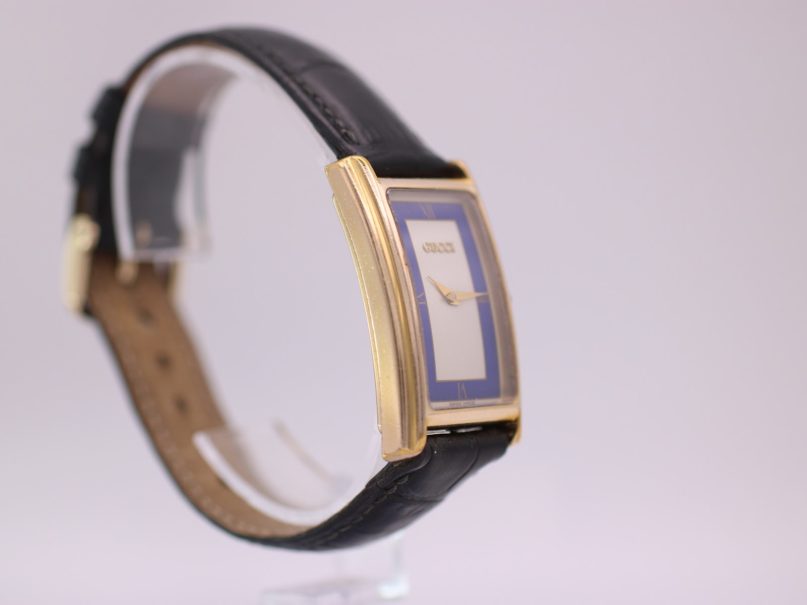 Angled side profile view of the Gucci 2600 M watch, highlighting the case curve and the black leather strap.