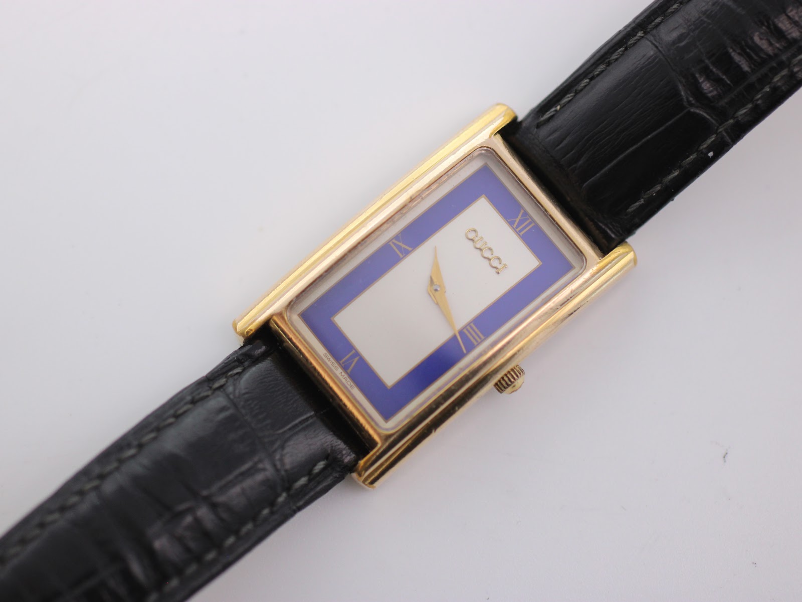 Top-down view of the rectangular gold-tone Gucci watch with its distinctive blue and white dial and black leather strap.