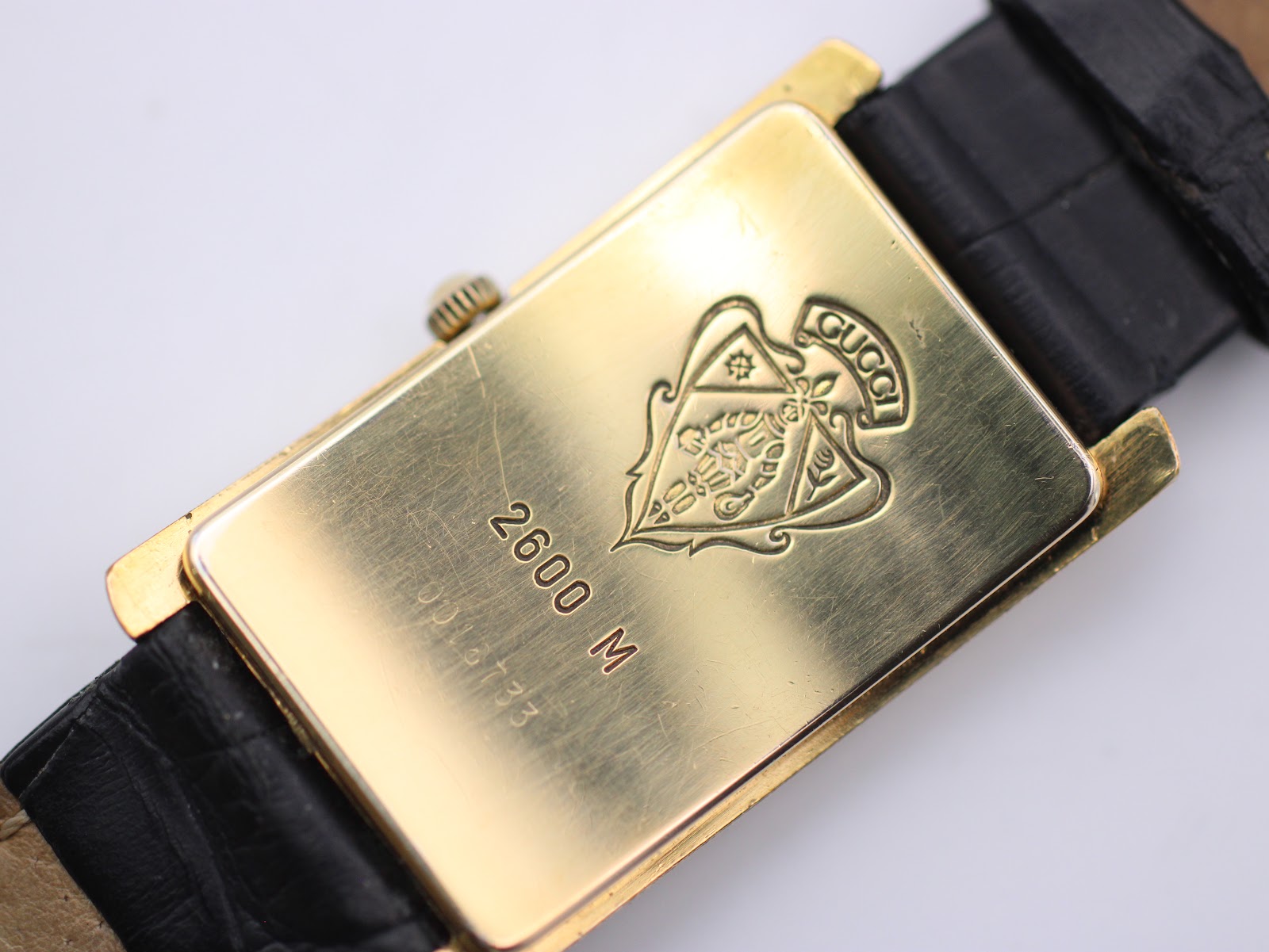 Close-up of the gold-tone case back of the Gucci 2600 M, showing engraved model number, serial number, and the Gucci crest logo.