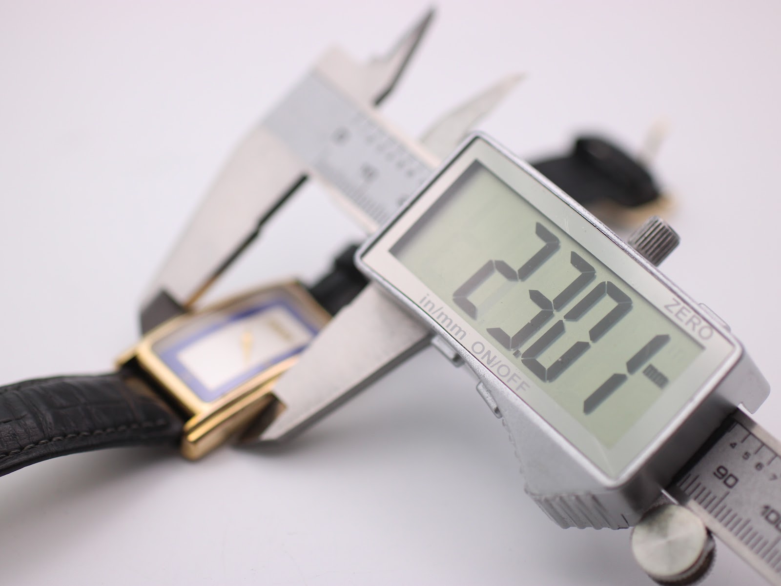 Digital caliper measuring the width of the Gucci watch case, displaying a precise measurement of 23.01 mm.