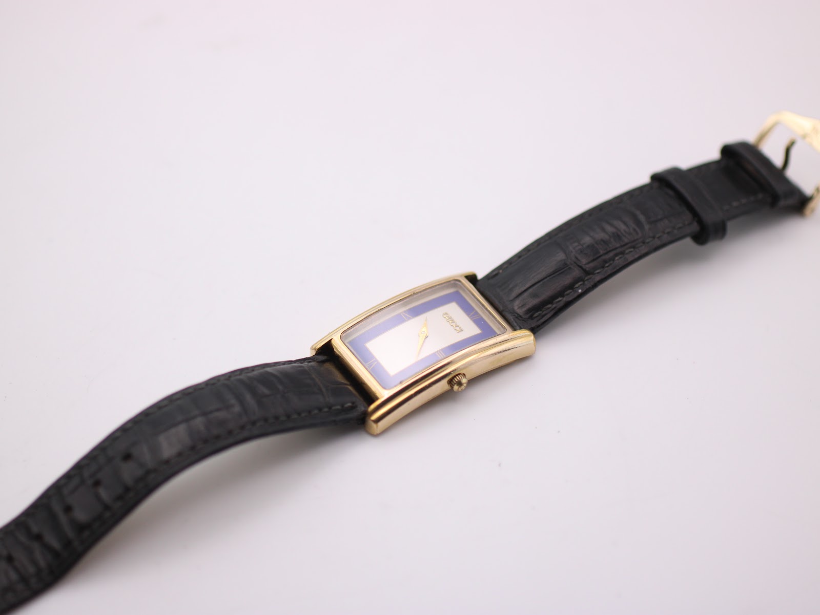 Full view of the Gucci watch from an angle, highlighting the black leather strap and the gold-tone buckle.