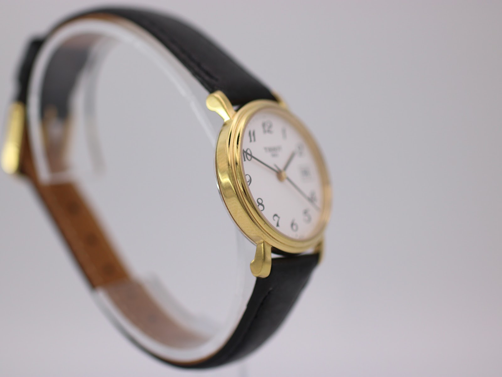Angled side view of the Tissot watch on a stand, highlighting the case profile and black leather strap.