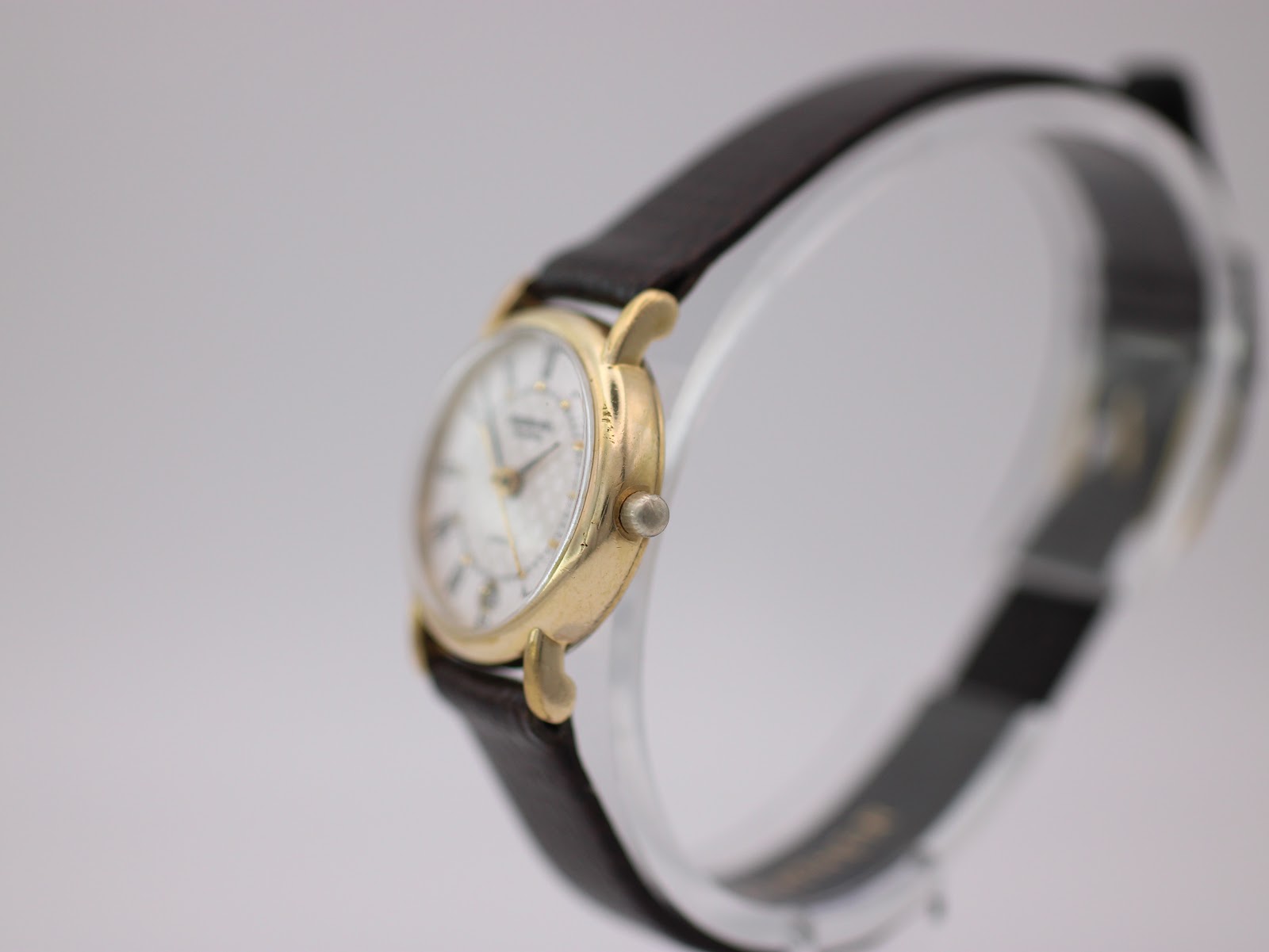 Angled side view of the watch on a display stand, showing the crown and case profile.