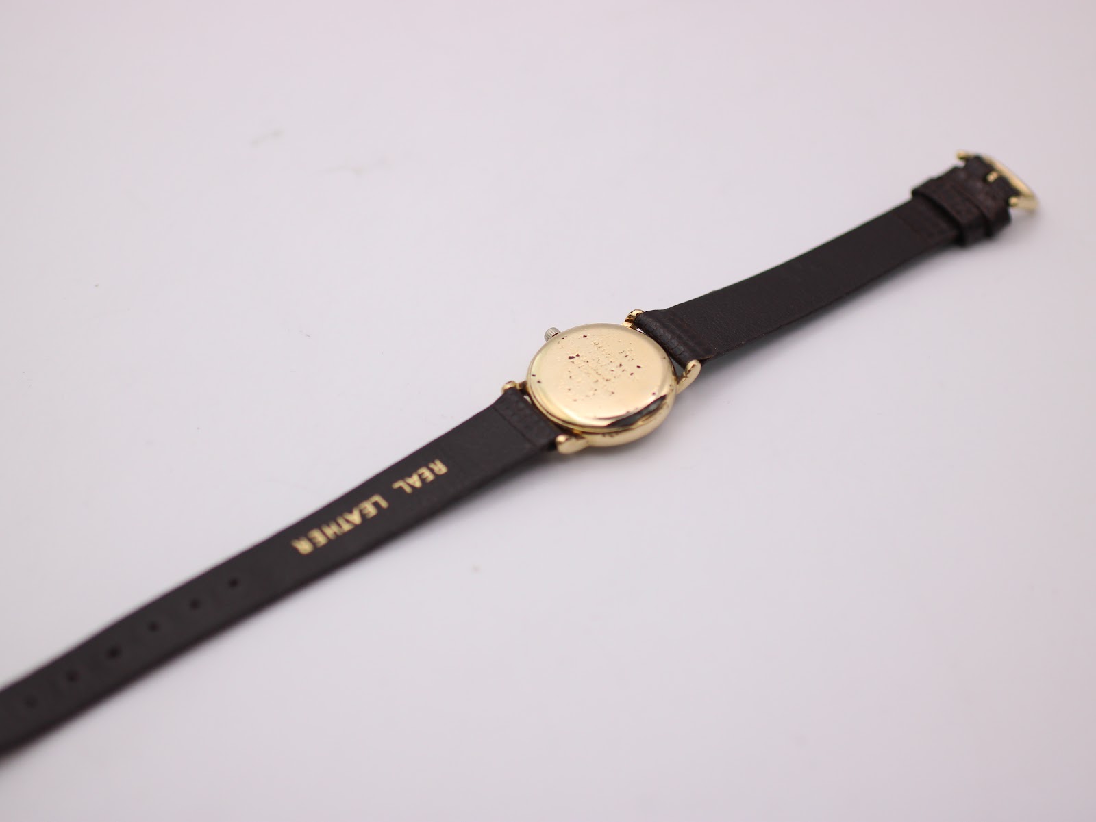 Rear view of the watch showing the plain gold-plated case back and the 'REAL LEATHER' marking on the strap.