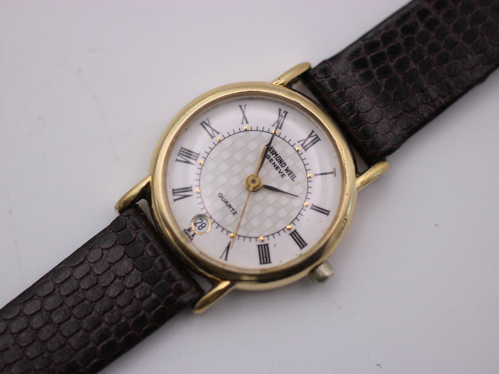Close-up shot of the white dial with Roman numerals, grid texture, and date window.