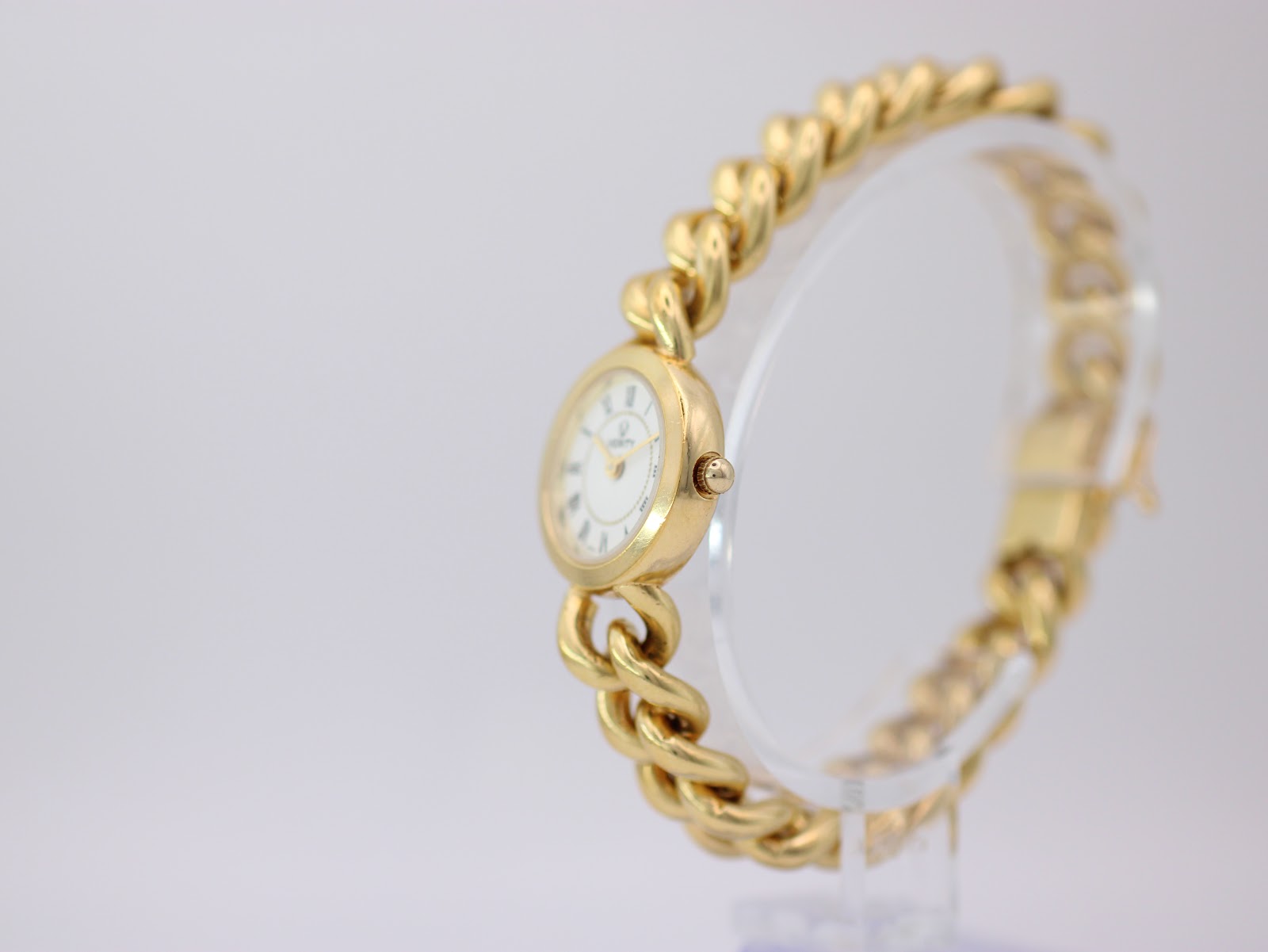 Side angled view of the Verity watch showing the polished gold-tone case and intricate chain link bracelet on a clear stand.