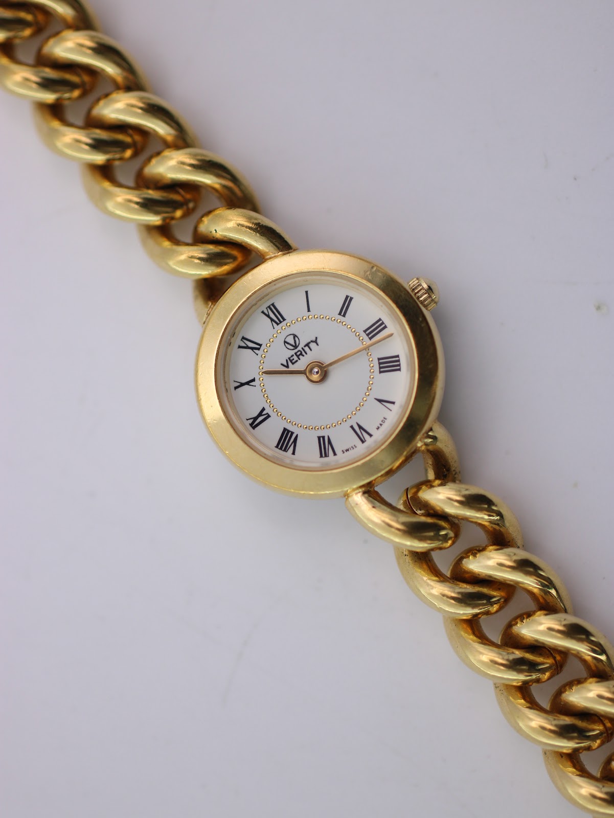 Close-up, slightly angled view of the Verity watch dial with black Roman numerals and gold-tone hands.