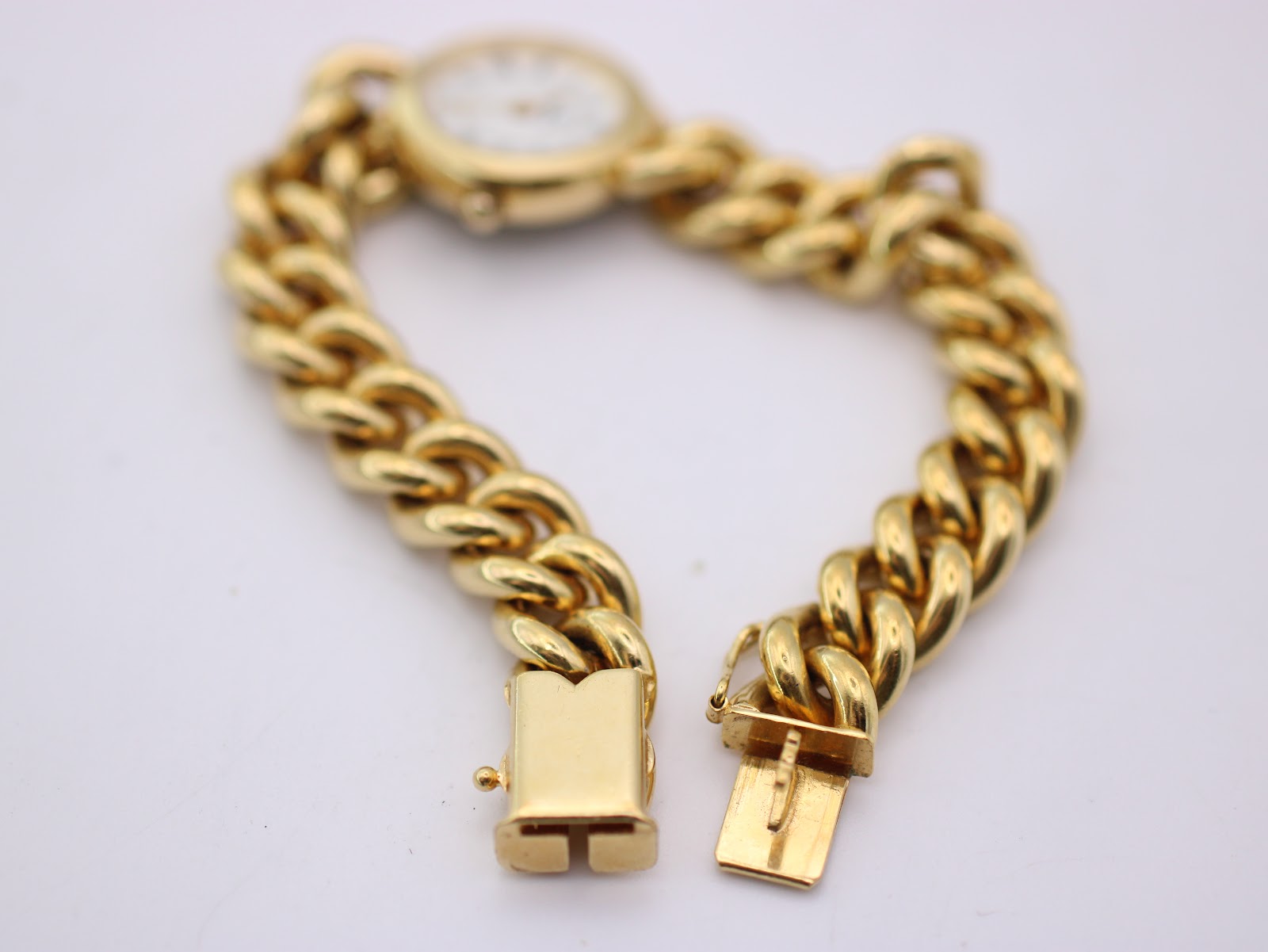 Close-up of the gold-tone fold-over clasp of the watch bracelet, open and ready to fasten.