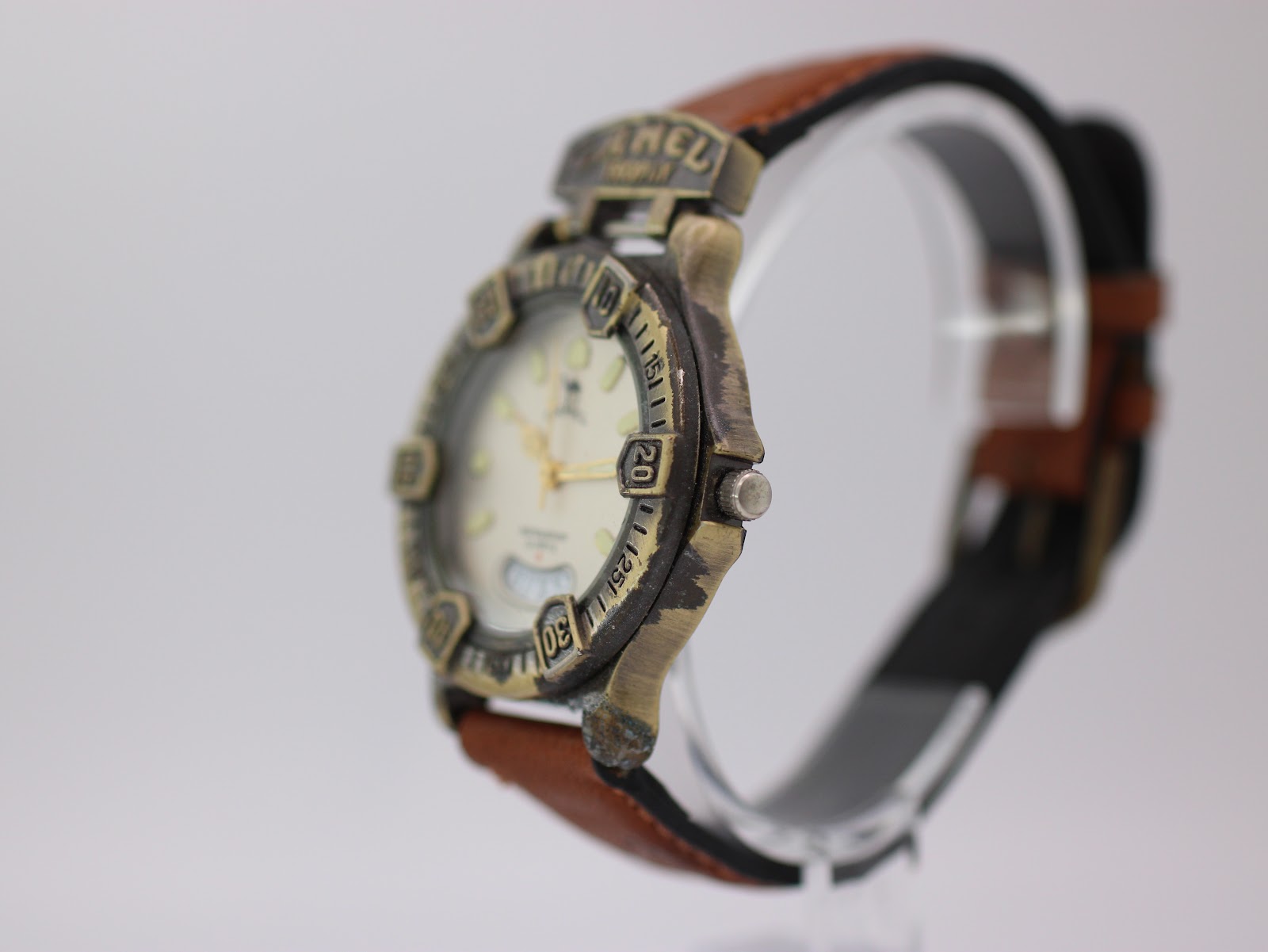 Angled side view of the Camel Trophy watch on a clear stand, highlighting the texture of the bronze-tone case and crown.