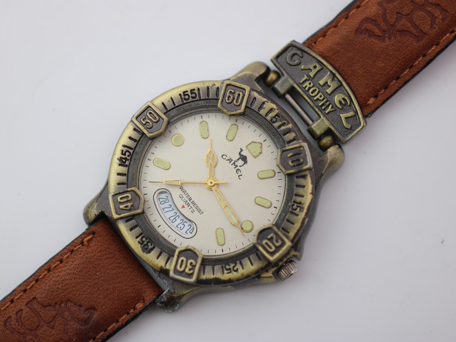 Close-up, angled view of the Camel Trophy watch dial, revealing the luminous markers, gold-tone hands, and multi-date display.