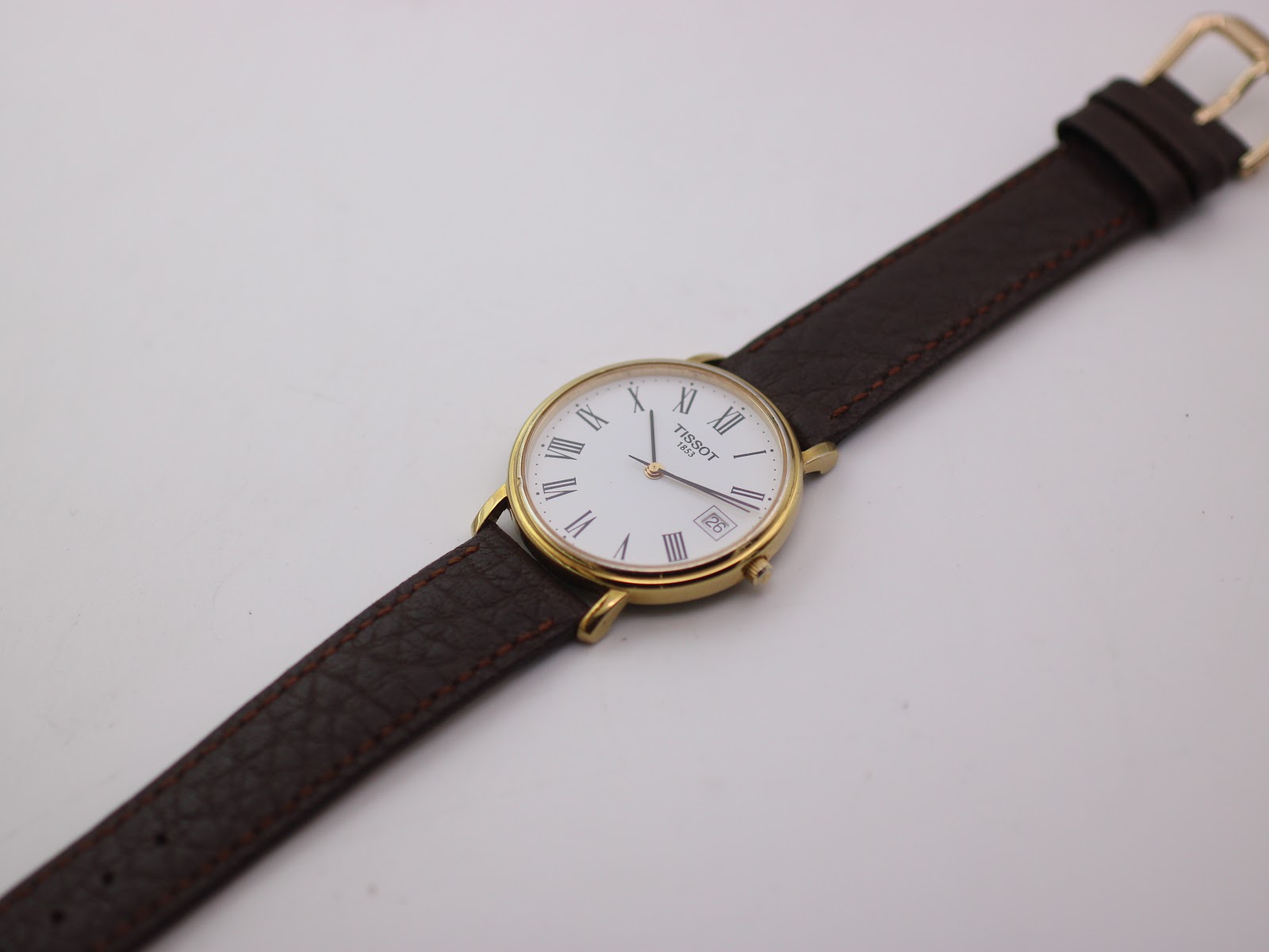 Overhead view of the Tissot watch with its brown leather strap extended on a white background.