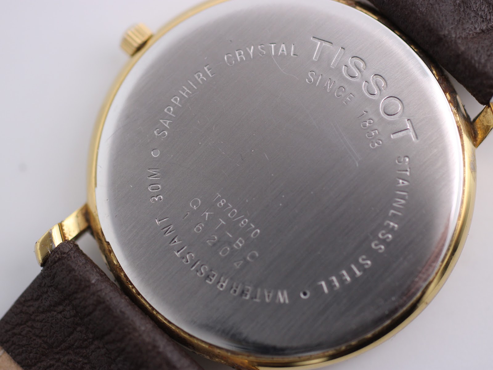 Extreme close-up of the stainless steel case back, showing 'TISSOT', 'SAPPHIRE CRYSTAL', '30M WATER RESISTANT', and model 'T870/970'.