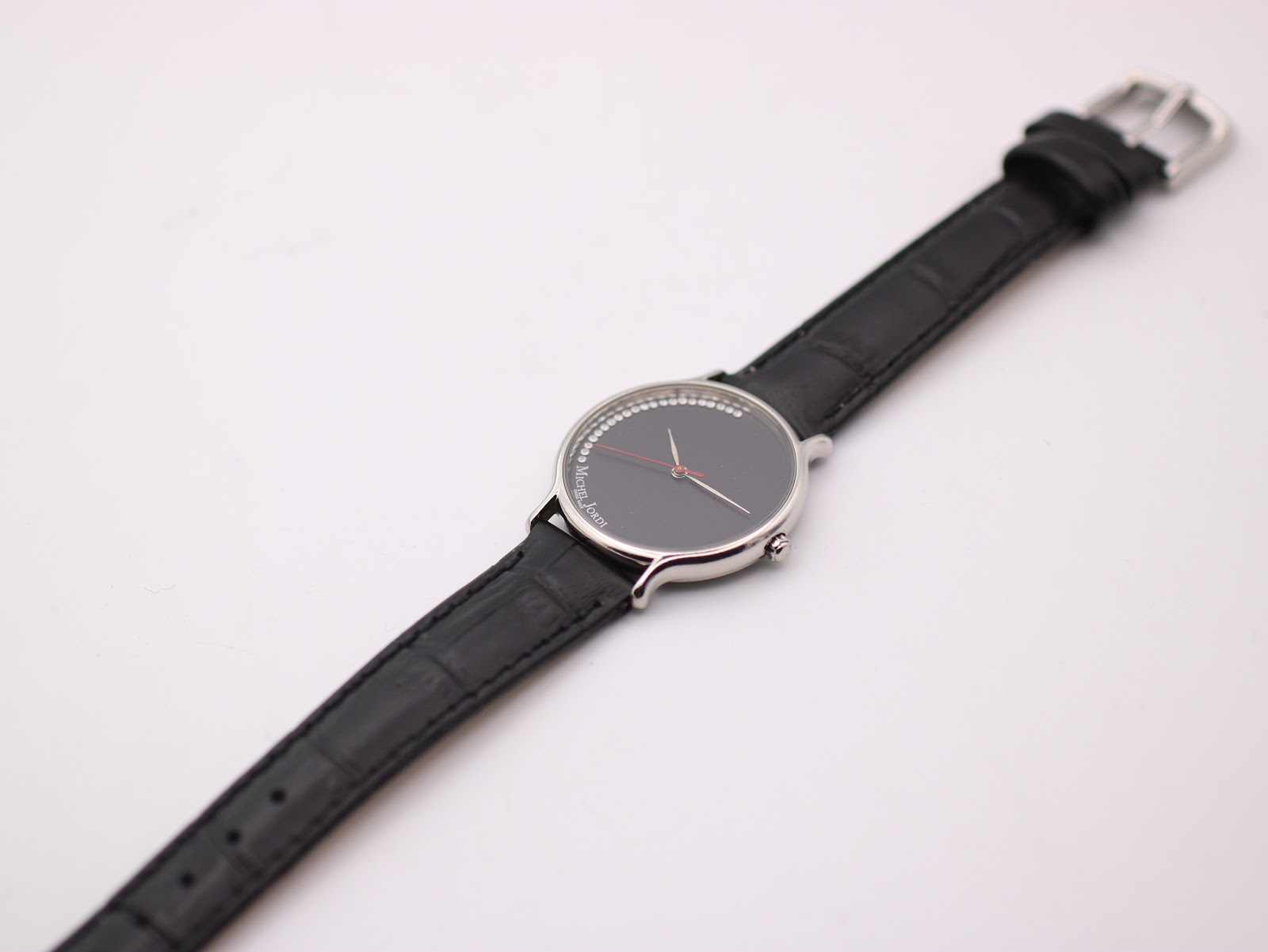 Top-down view of the Michel Jordi watch with its black leather strap laid flat.