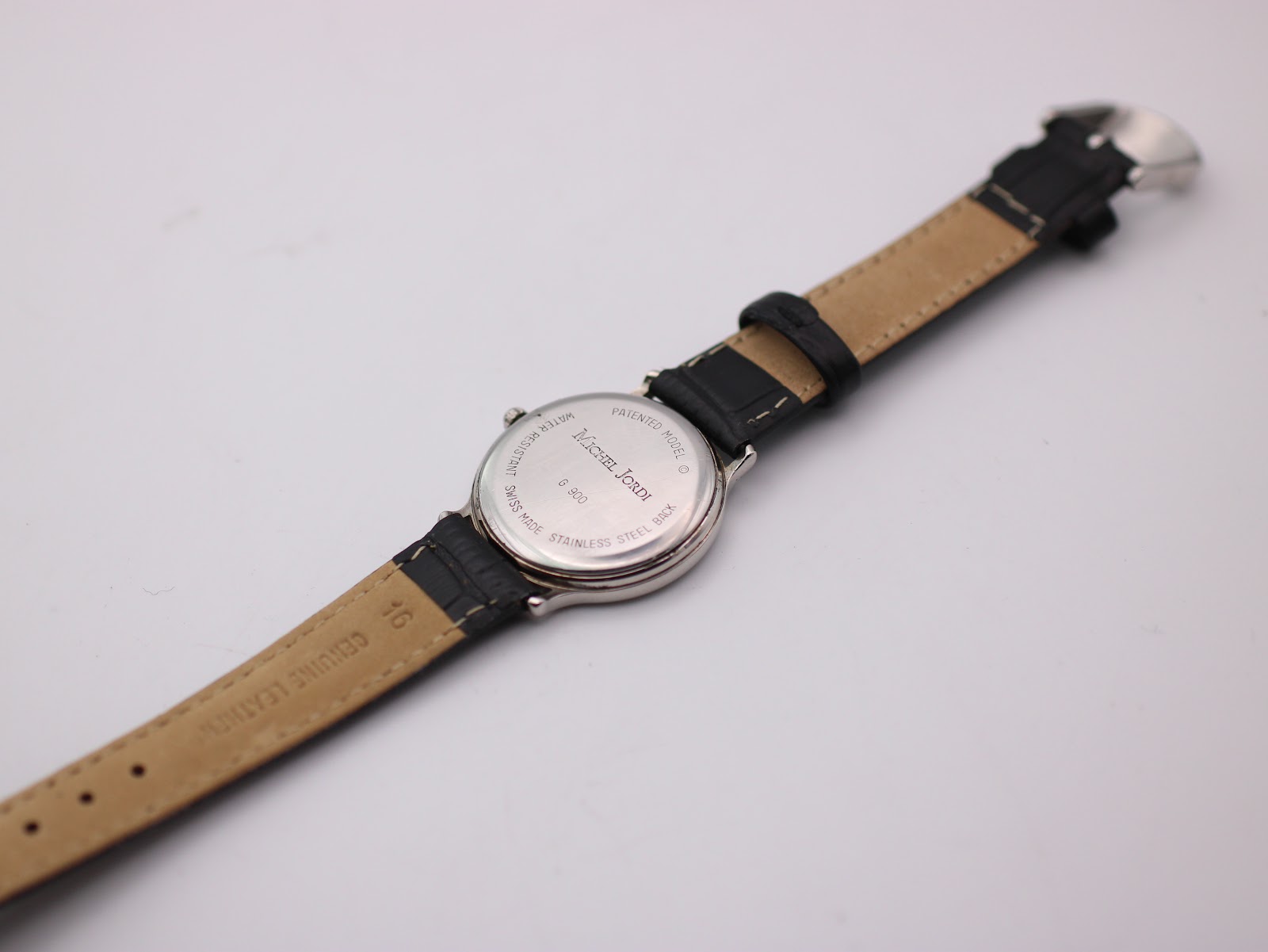 Case back of the Michel Jordi G 900 watch showing "Swiss Made Stainless Steel Back Water Resistant" engravings and "Genuine Leather" on the strap.