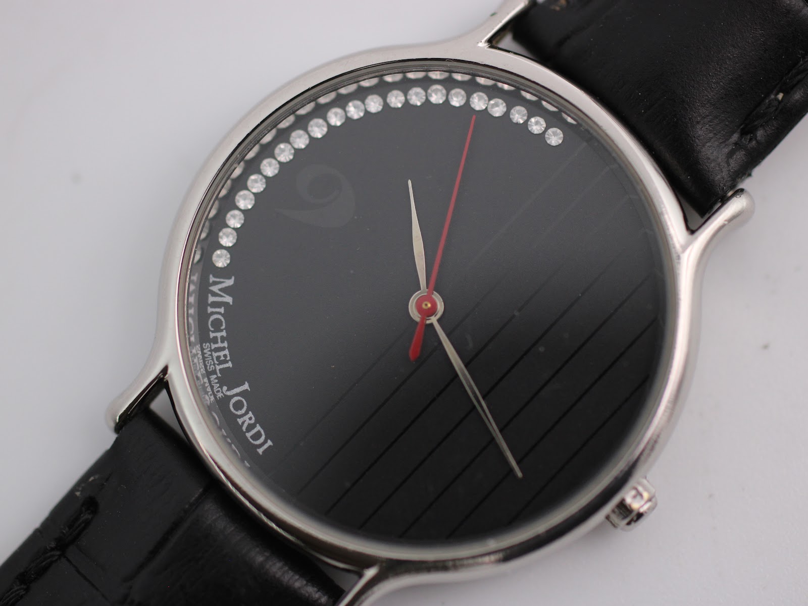 Close-up of the black dial with crystal hour markers, red seconds hand, and "Michel Jordi Swiss Made" logo.