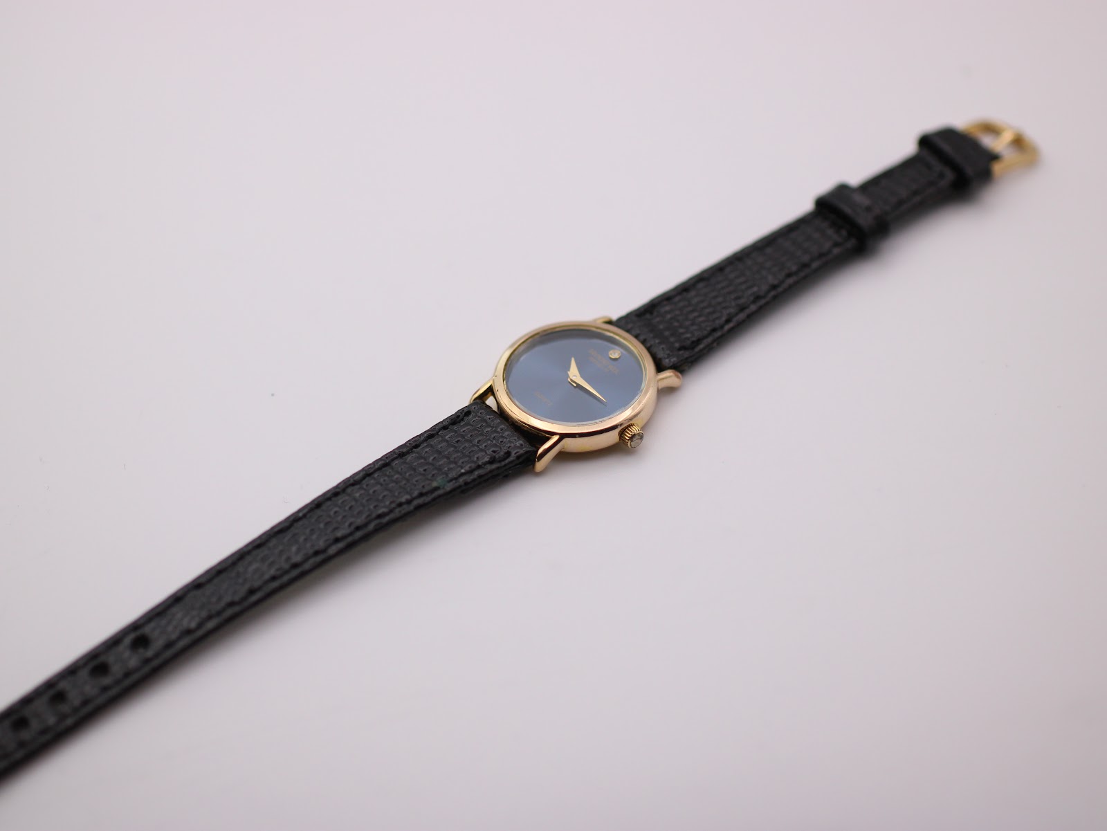 Overhead shot of the Raymond Weil watch laid flat, displaying the full length of the black textured leather strap and gold buckle.
