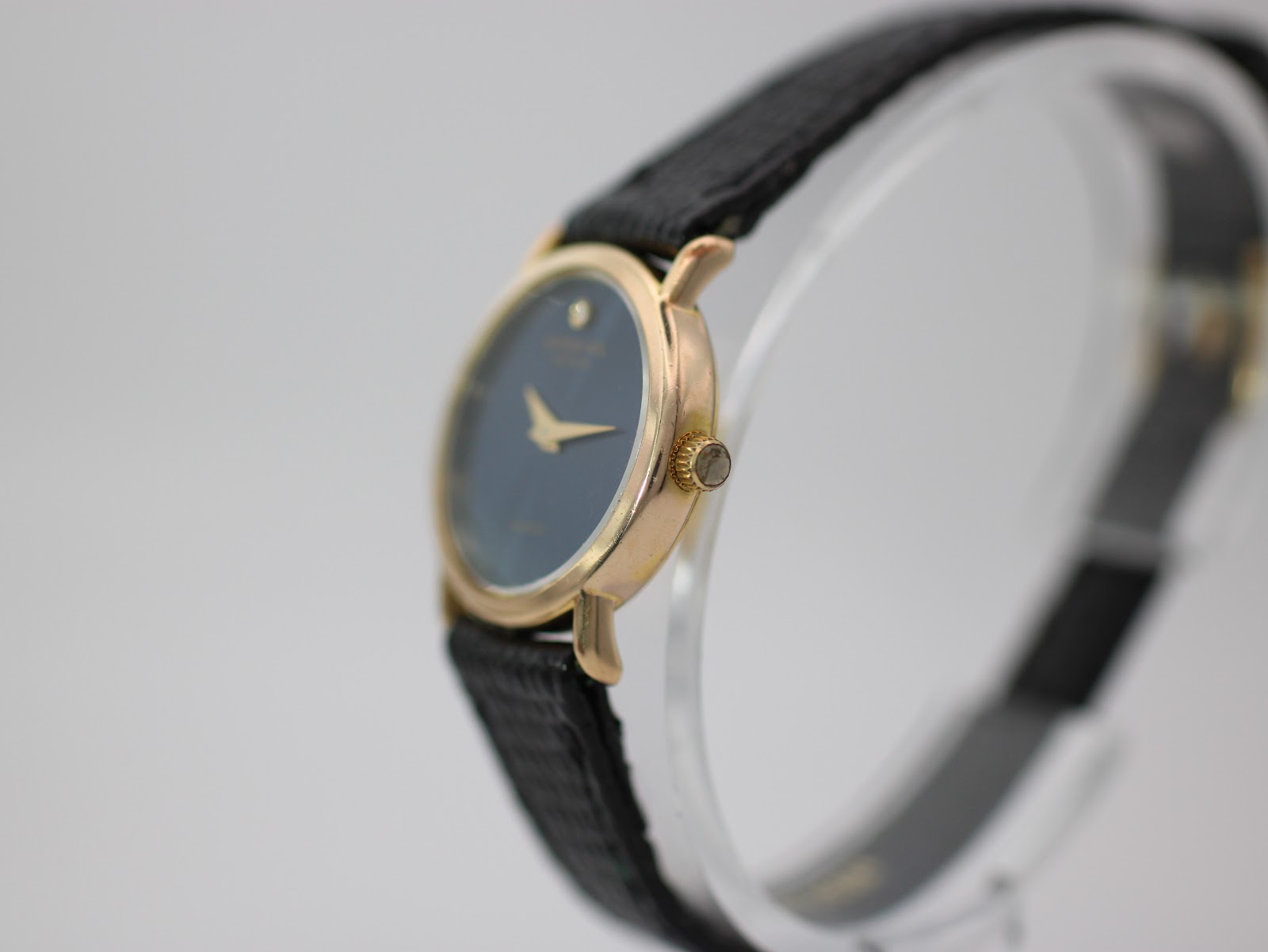 Angled side view of Raymond Weil 5758 watch showing gold tone case, crown, and black textured leather strap.