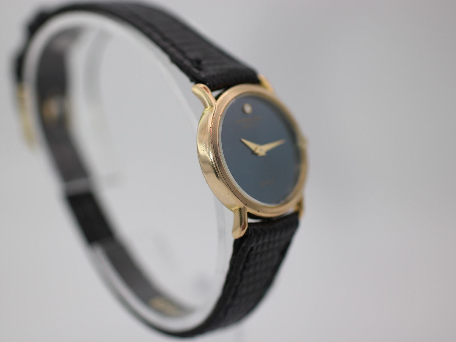 Three-quarter view of the Raymond Weil watch from the side, highlighting the slim profile of the gold case and black strap.