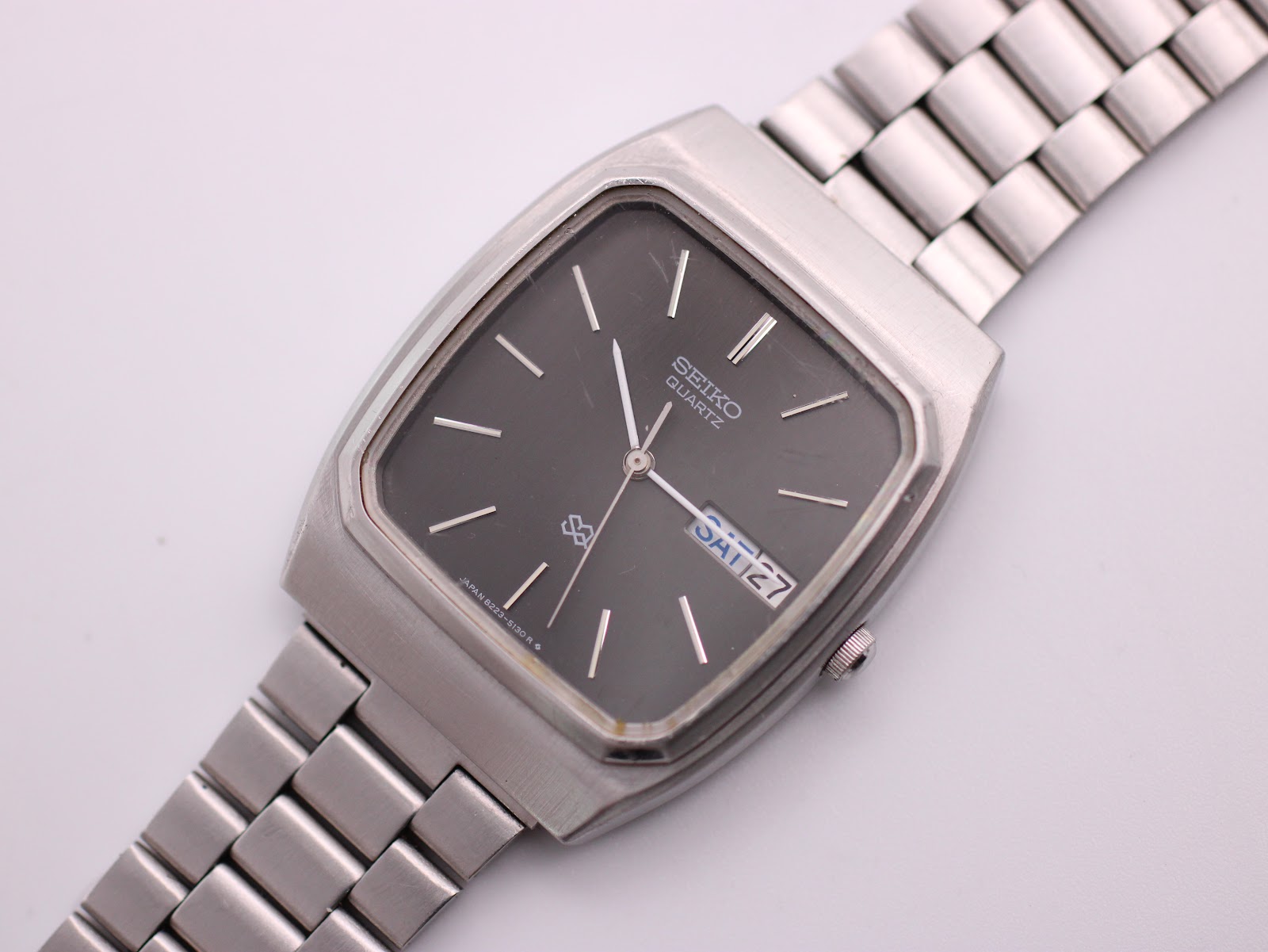Angled close-up of the Seiko watch dial, showing the black face, baton indices, and day-date window.